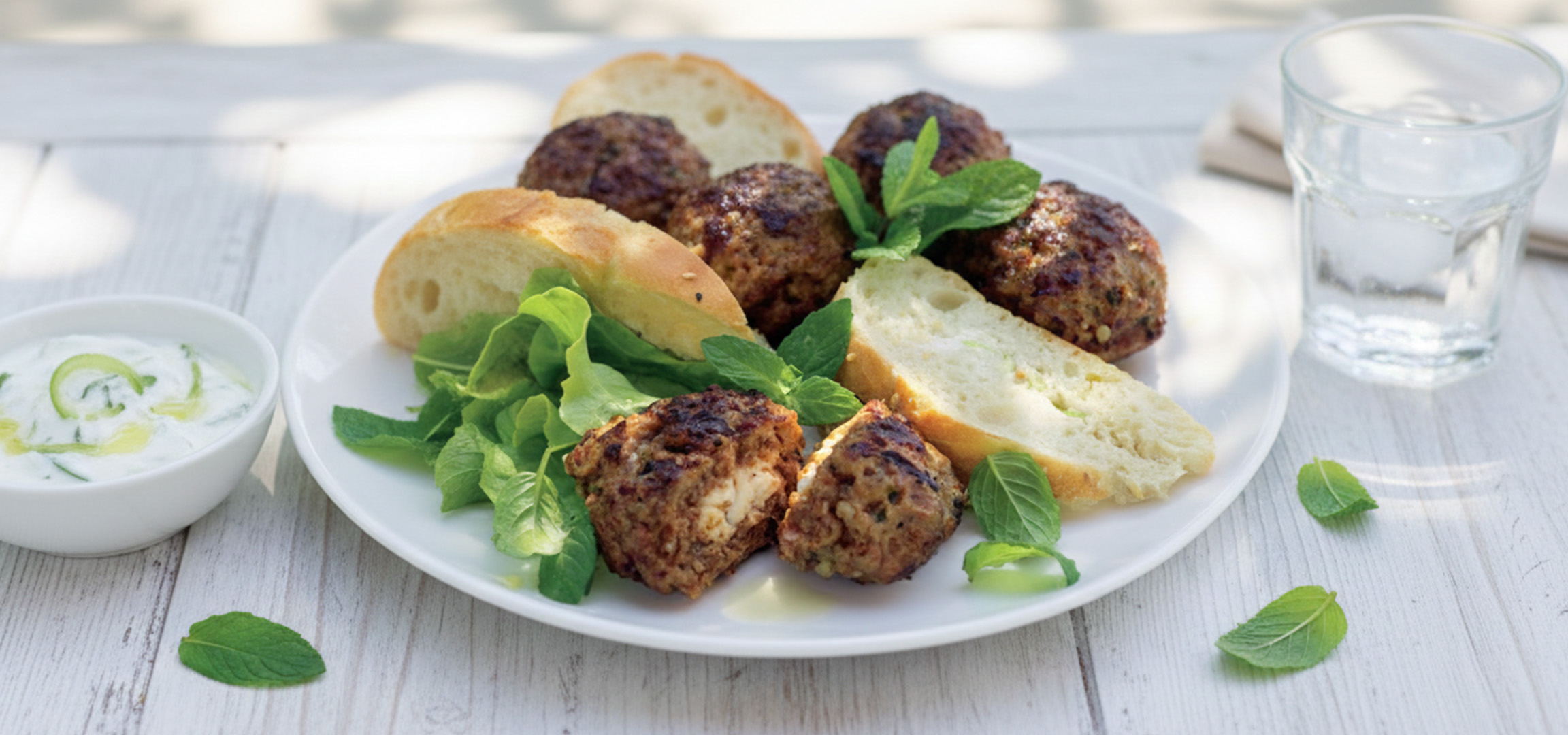 Boulettes de viande avec de la salade, du pain et une sauce au yaourt.