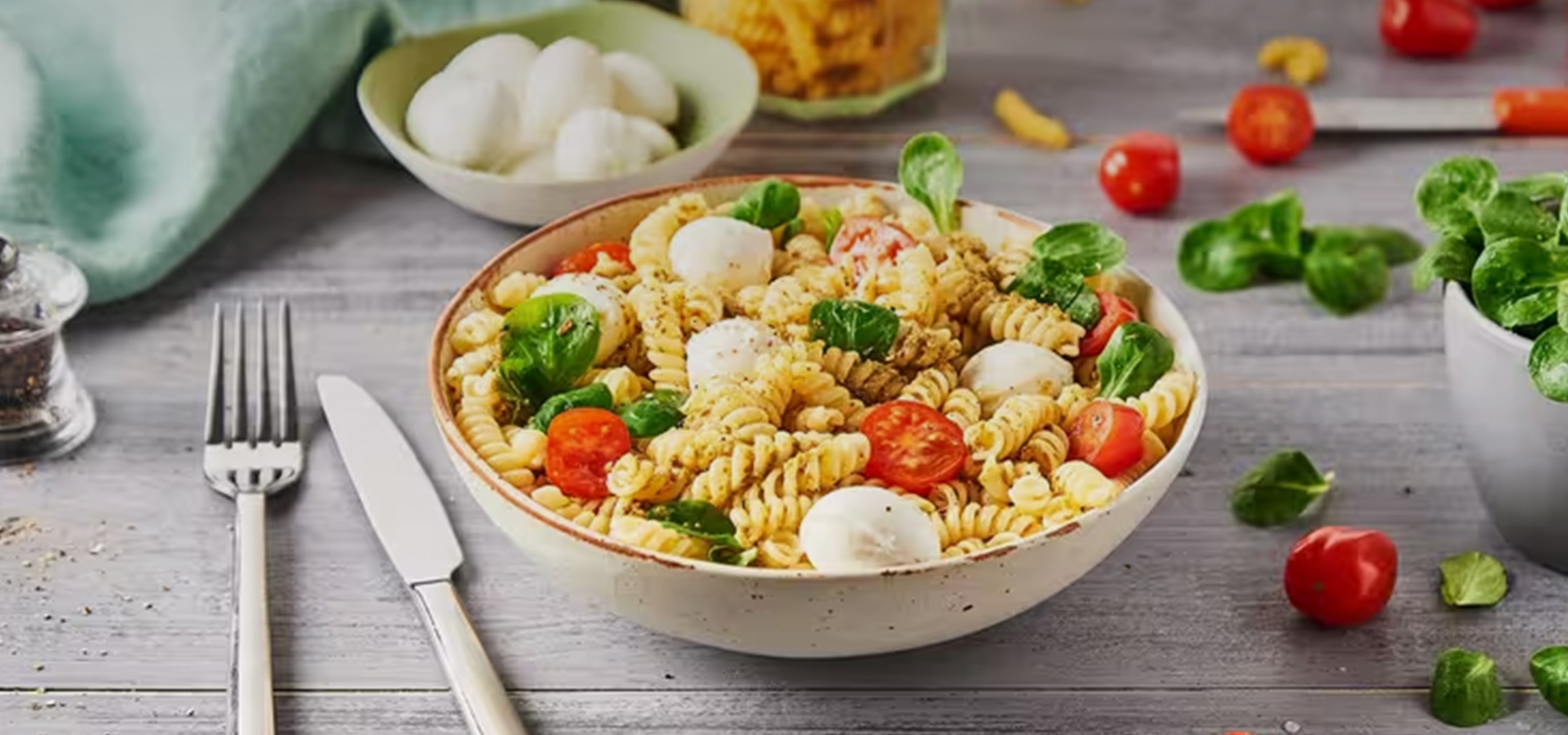 Salade de pâtes fusilli avec tomates cerises, mozzarella et basilic frais sur une table en bois.