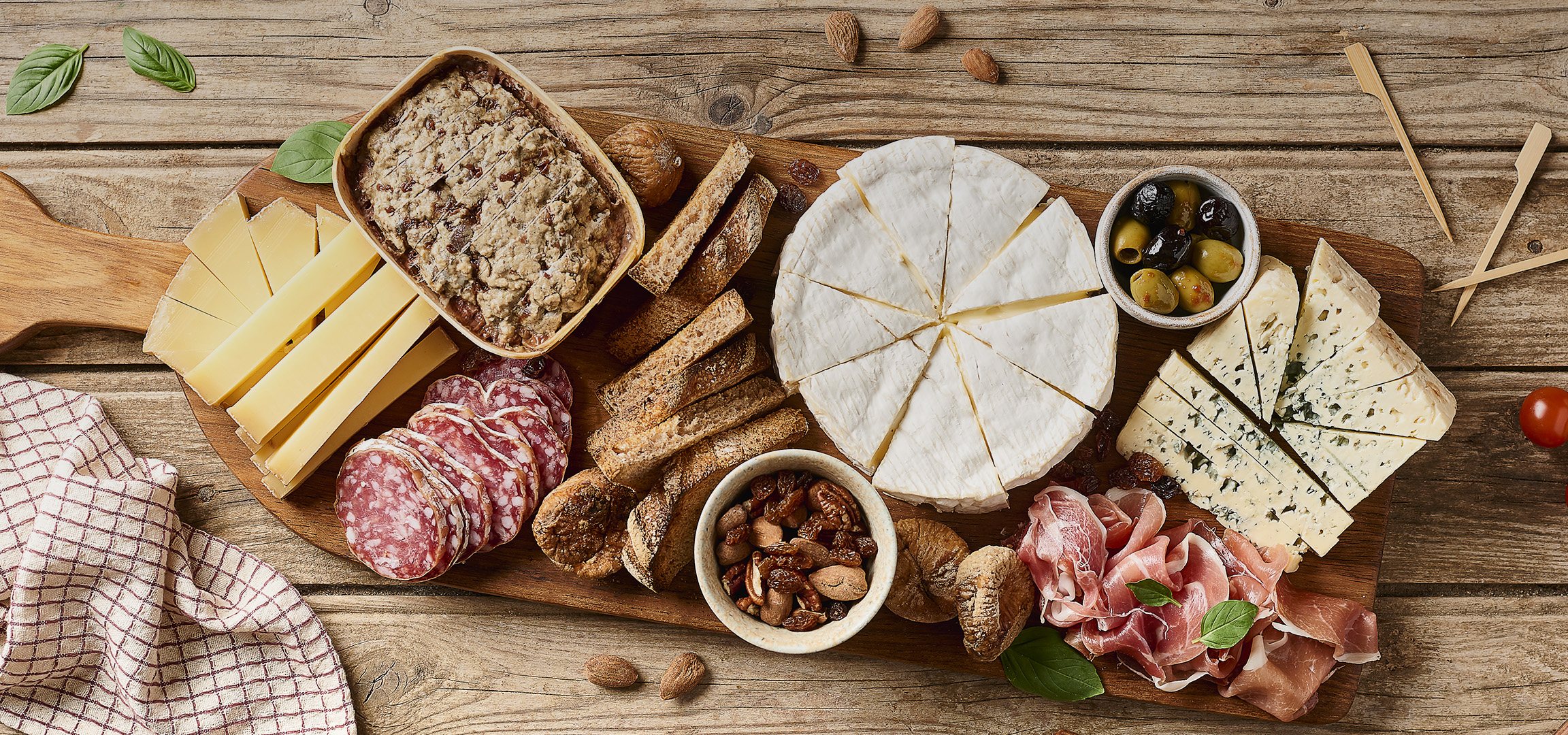 Plateau de fromages et charcuteries avec du brie, du fromage bleu, du salami, du jambon, des olives et des tomates cerises.