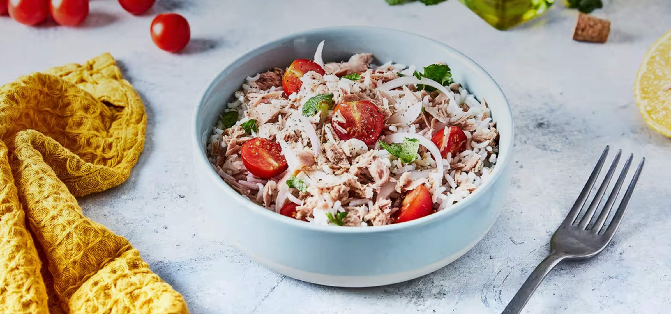 Salade de riz au thon, tomates cerises, oignons et persil, avec un torchon jaune et un citron.