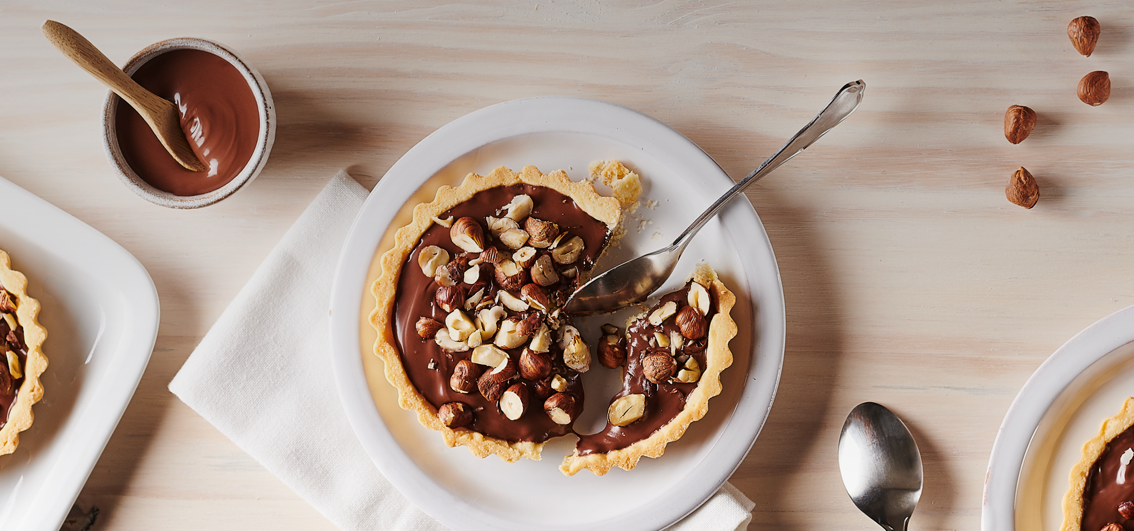 Tartelettes au chocolat et aux noisettes sur une table en bois clair.