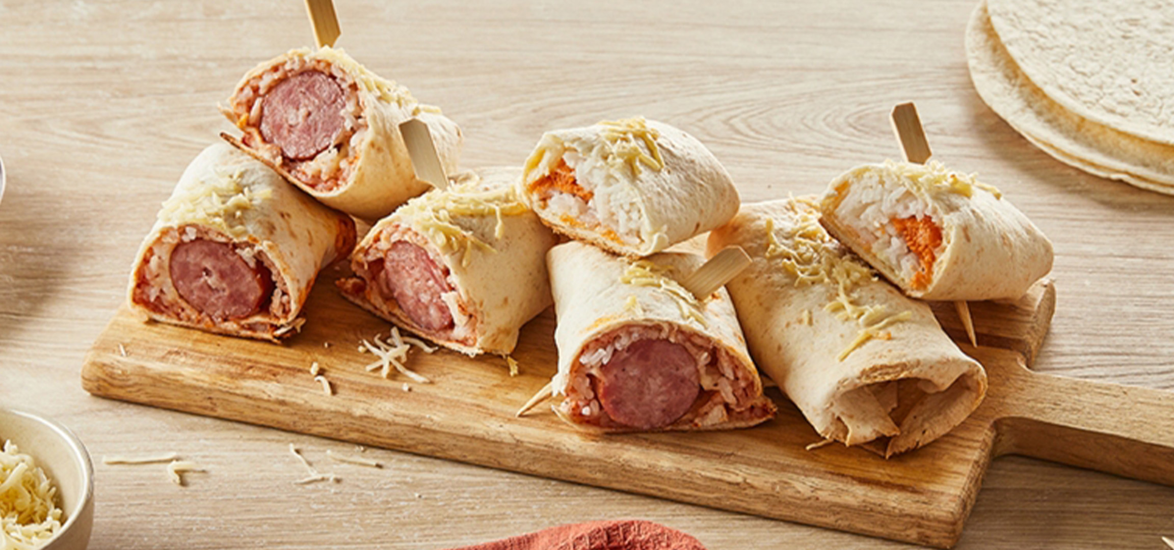 Wraps de saucisses coupés en deux avec du fromage râpé sur une planche en bois.