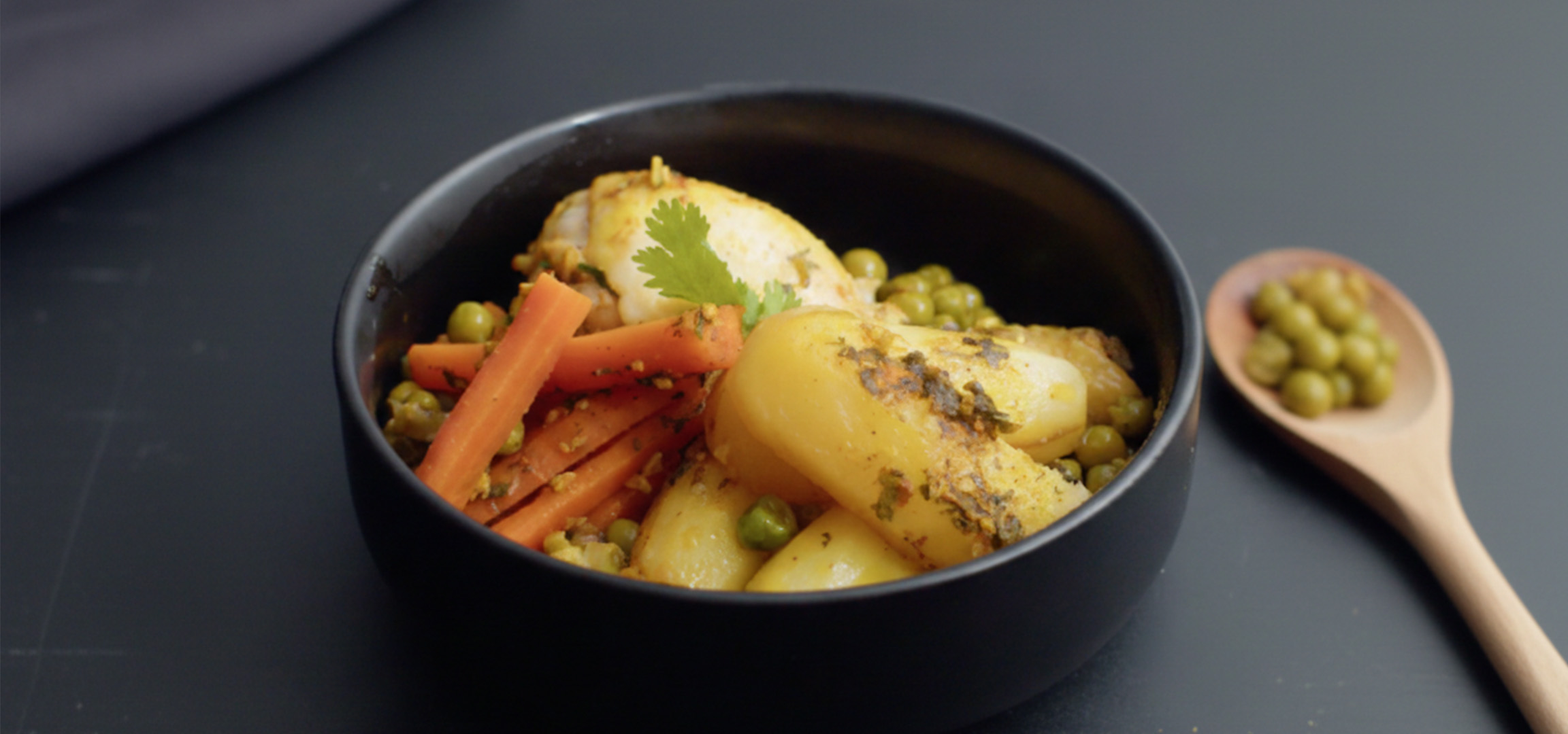 Plat de poulet, pommes de terre, carottes et petits pois, garni de coriandre.