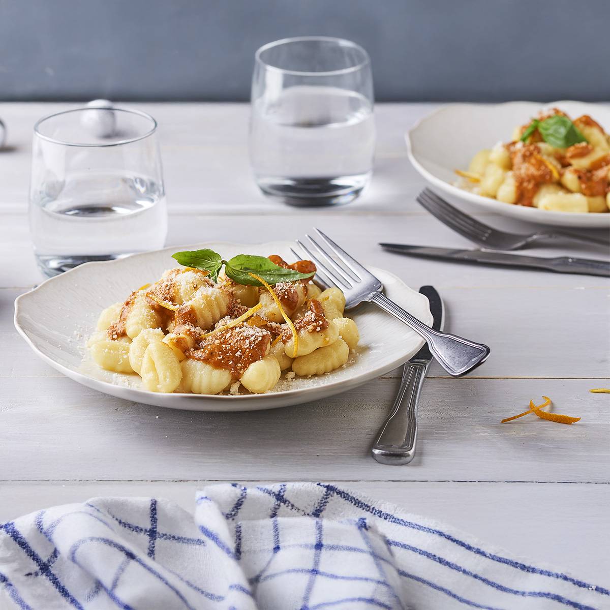 Deux assiettes de gnocchis avec sauce, fromage et basilic, accompagnées de verres d'eau.