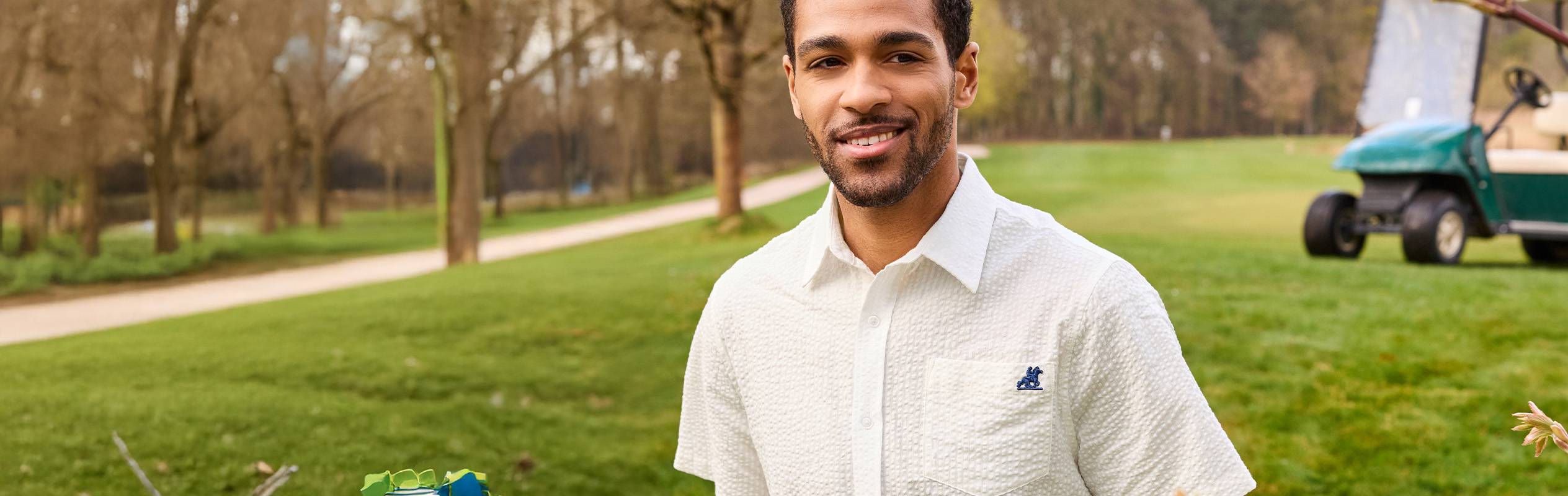 Un homme souriant porte une chemise blanche à motif gaufré sur un terrain de golf.