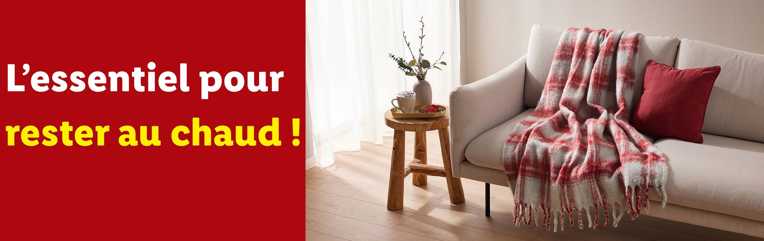 Un canapé avec un plaid à carreaux rouges et blancs, un coussin rouge et une table d'appoint en bois.