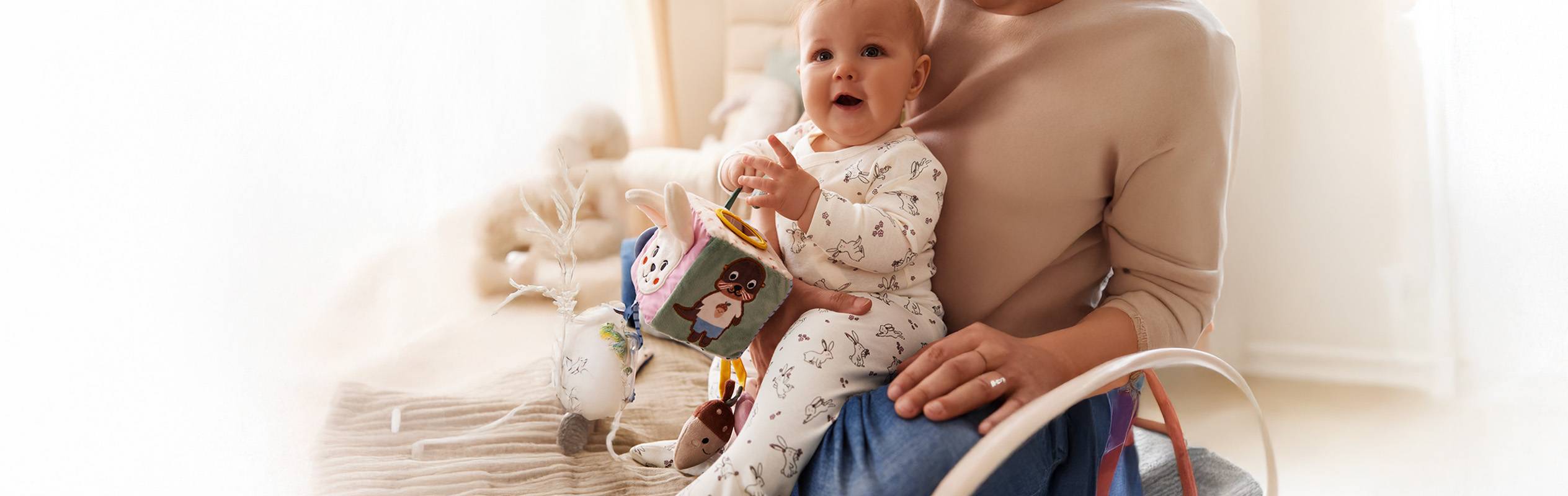Un bébé joue avec un cube d'activités en tissu de la marque Sterntaler, assis sur les genoux de sa mère.