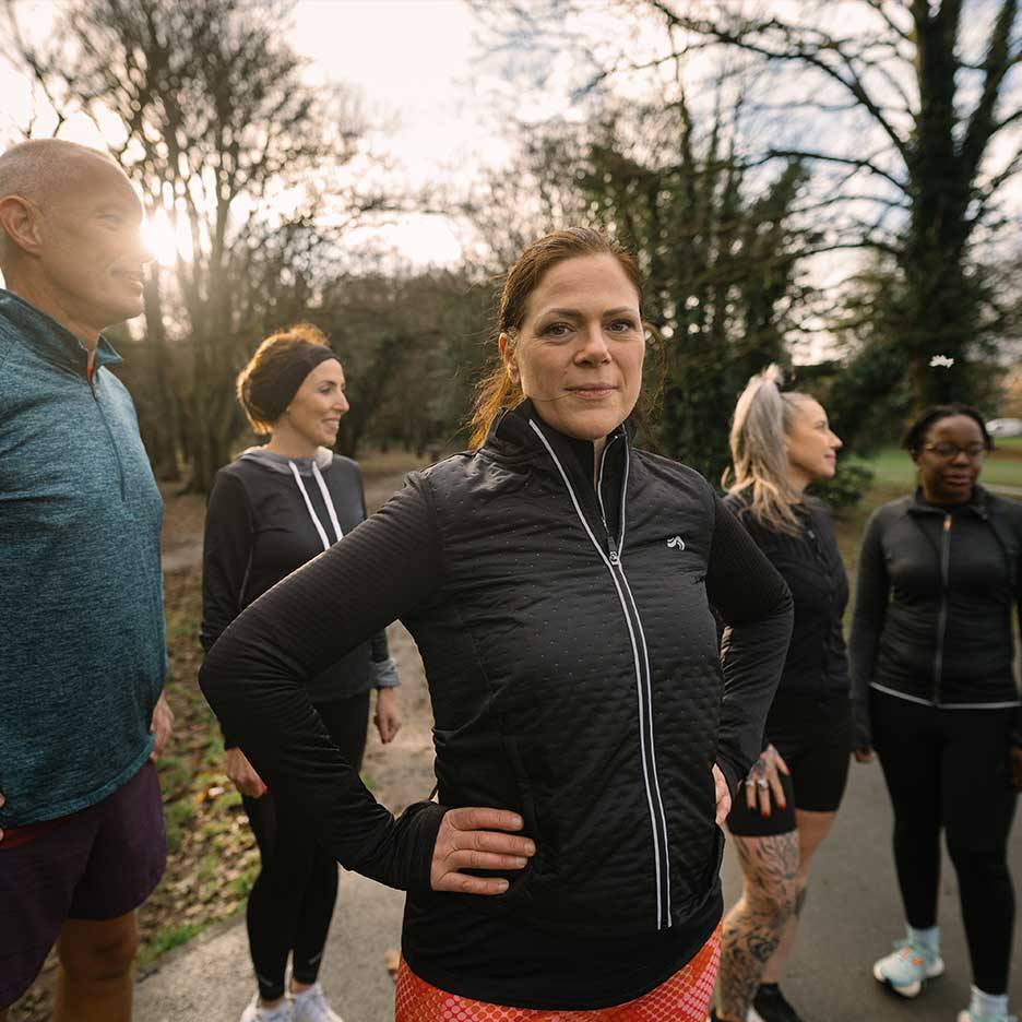 Groupe de personnes en tenue de sport, dont une femme en veste matelassée noire, en extérieur.