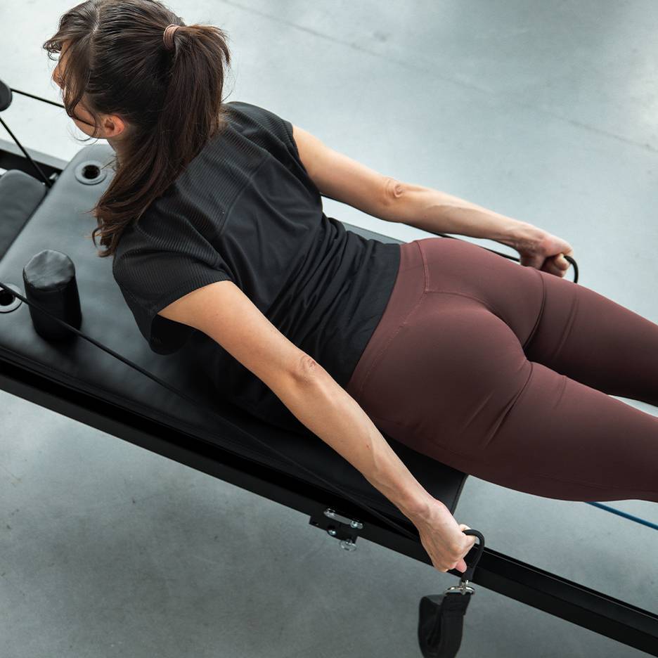 Femme faisant de l'exercice sur un appareil de Pilates avec des bandes de résistance, vêtue de vêtements de sport.