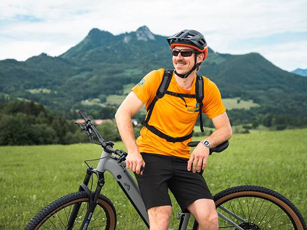 Un homme souriant, portant un casque et des lunettes de soleil, est assis sur un vélo électrique Haibike dans un paysage montagneux.