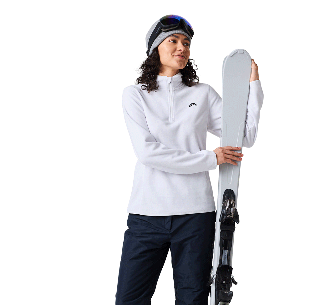Femme en polaire blanche et pantalon de ski bleu marine tenant un ski.