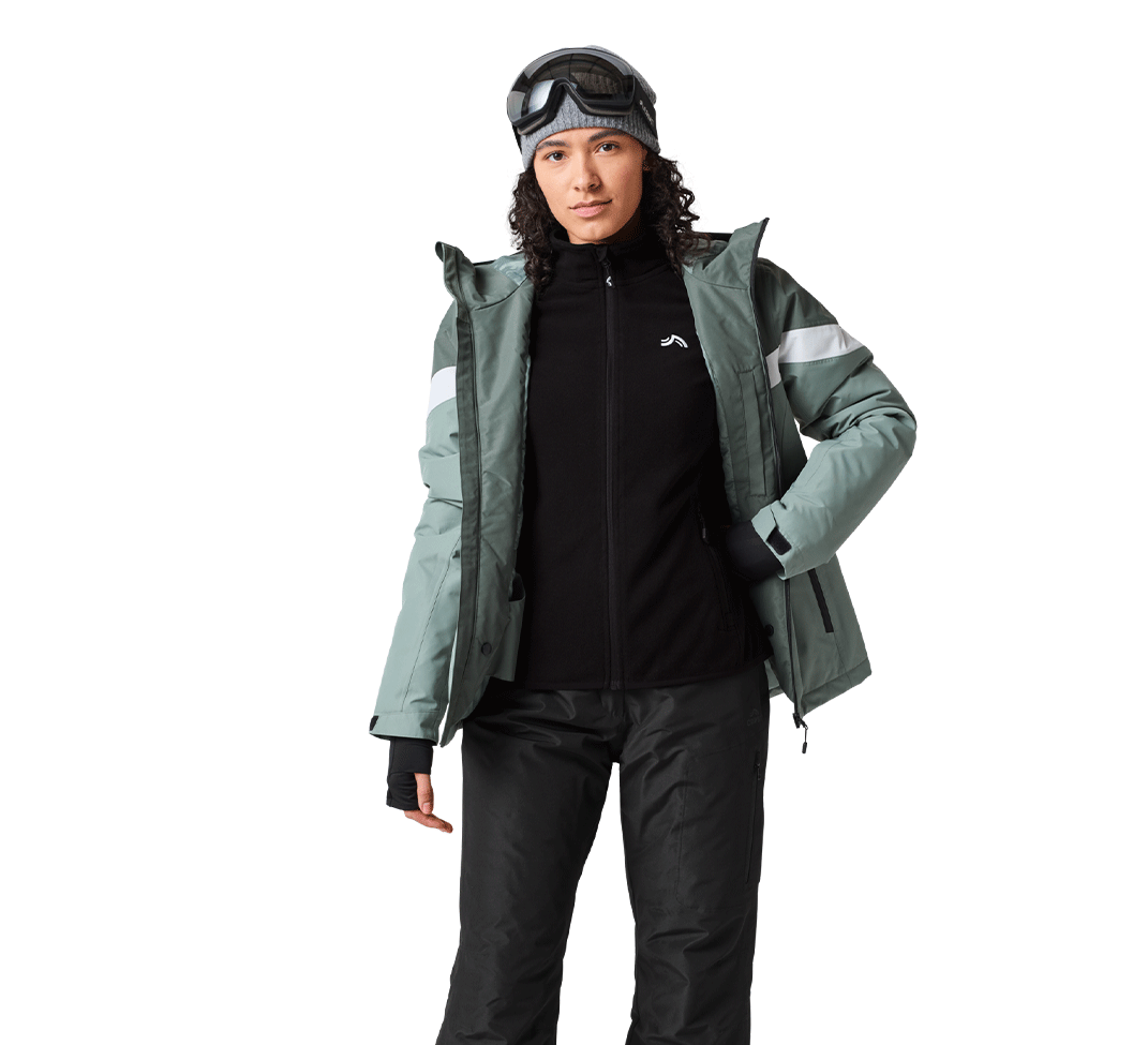 Femme en tenue de ski avec veste vert sauge, polaire noire et bonnet gris.