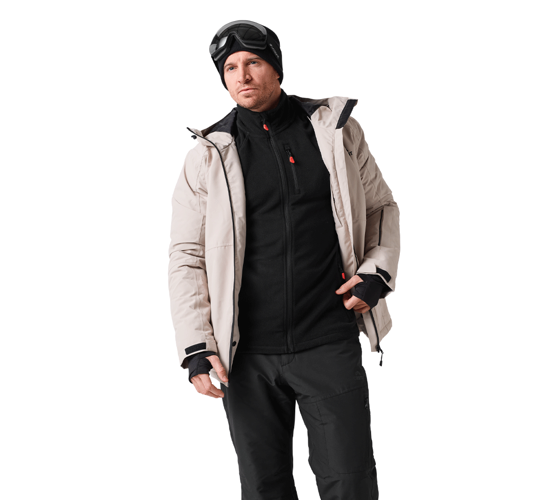 Homme en tenue de ski avec veste beige, polaire noire et pantalon de ski noir.