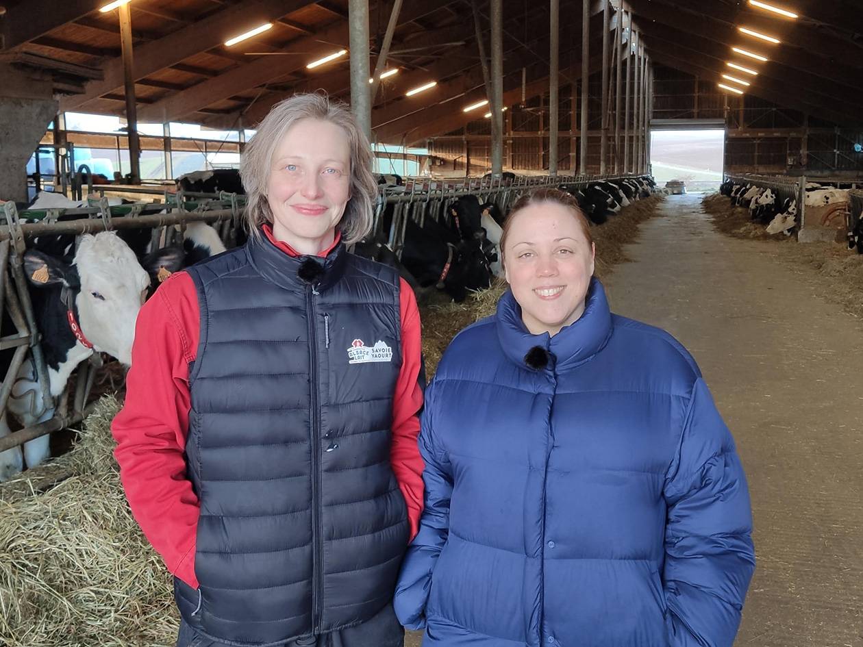 Deux femmes souriantes dans une étable avec des vaches laitières.