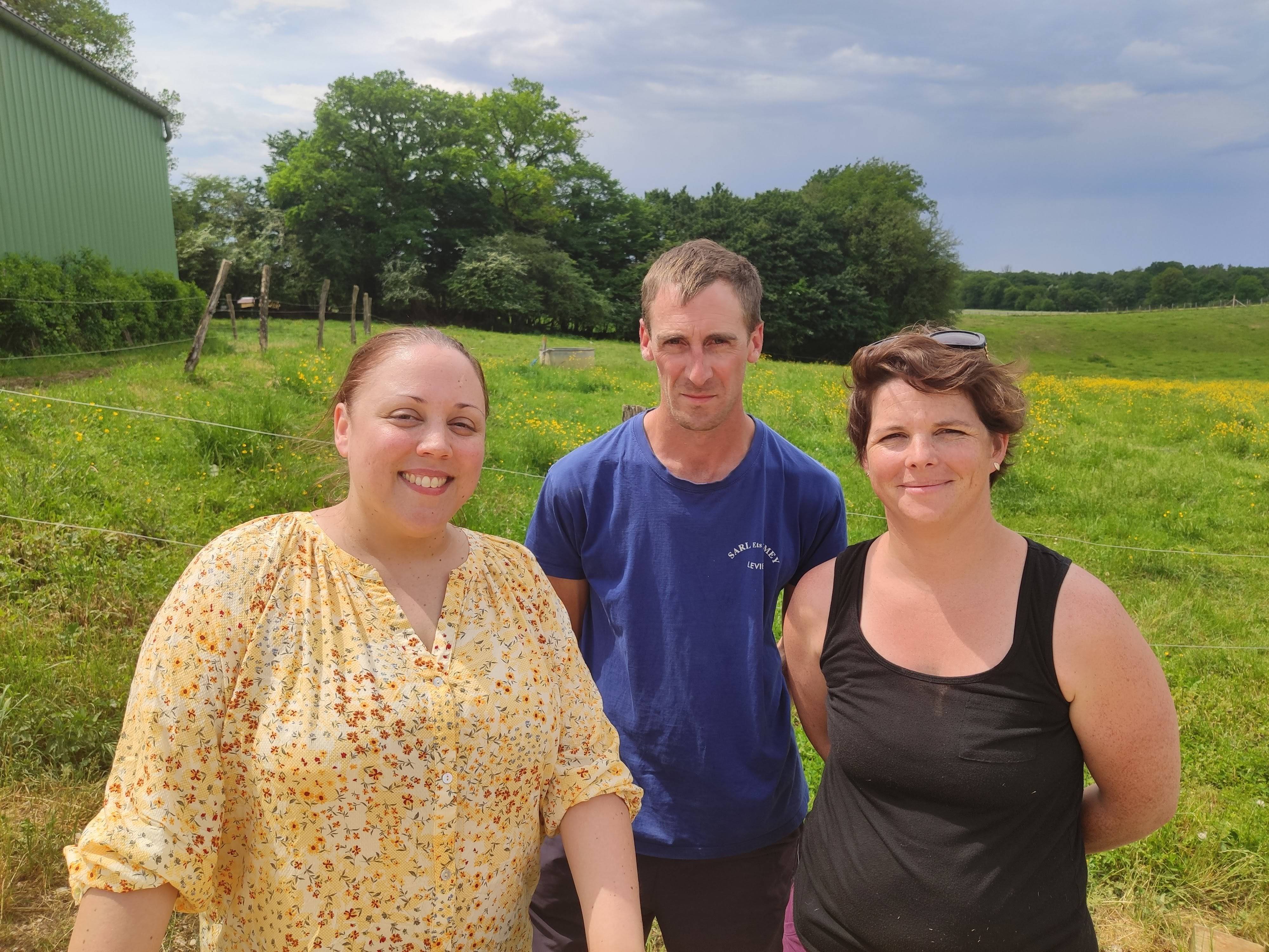 Trois personnes debout dans un champ avec de l'herbe verte et des arbres en arrière-plan.