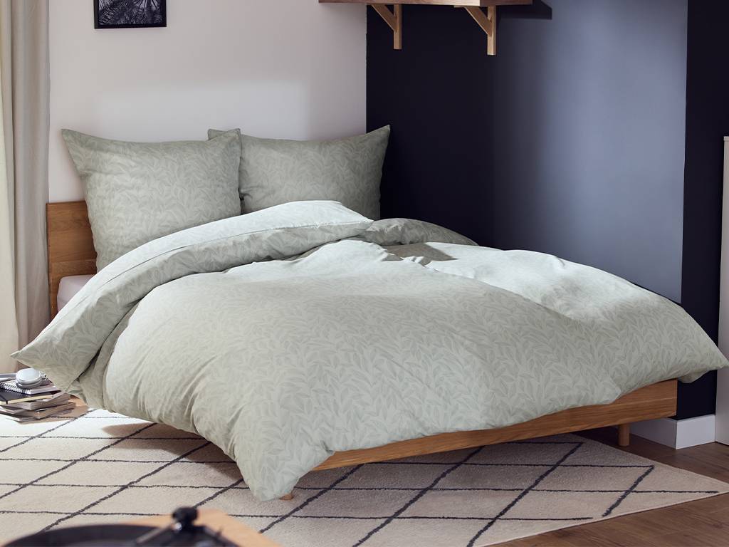 Parure de lit vert clair à motifs de feuilles sur un lit en bois dans une chambre moderne.