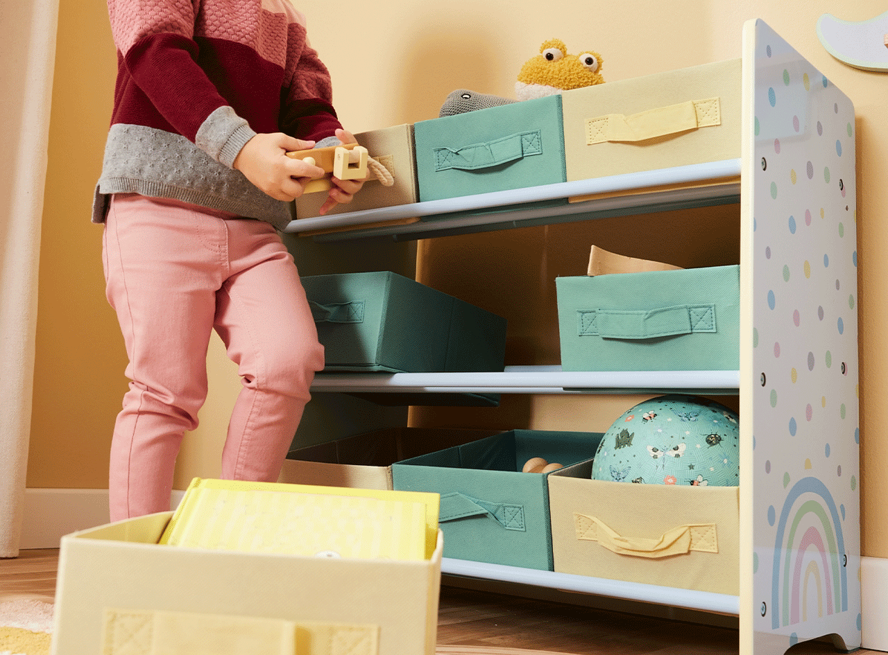 Enfant jouant avec un jouet en bois près d'une étagère de rangement avec des bacs colorés.