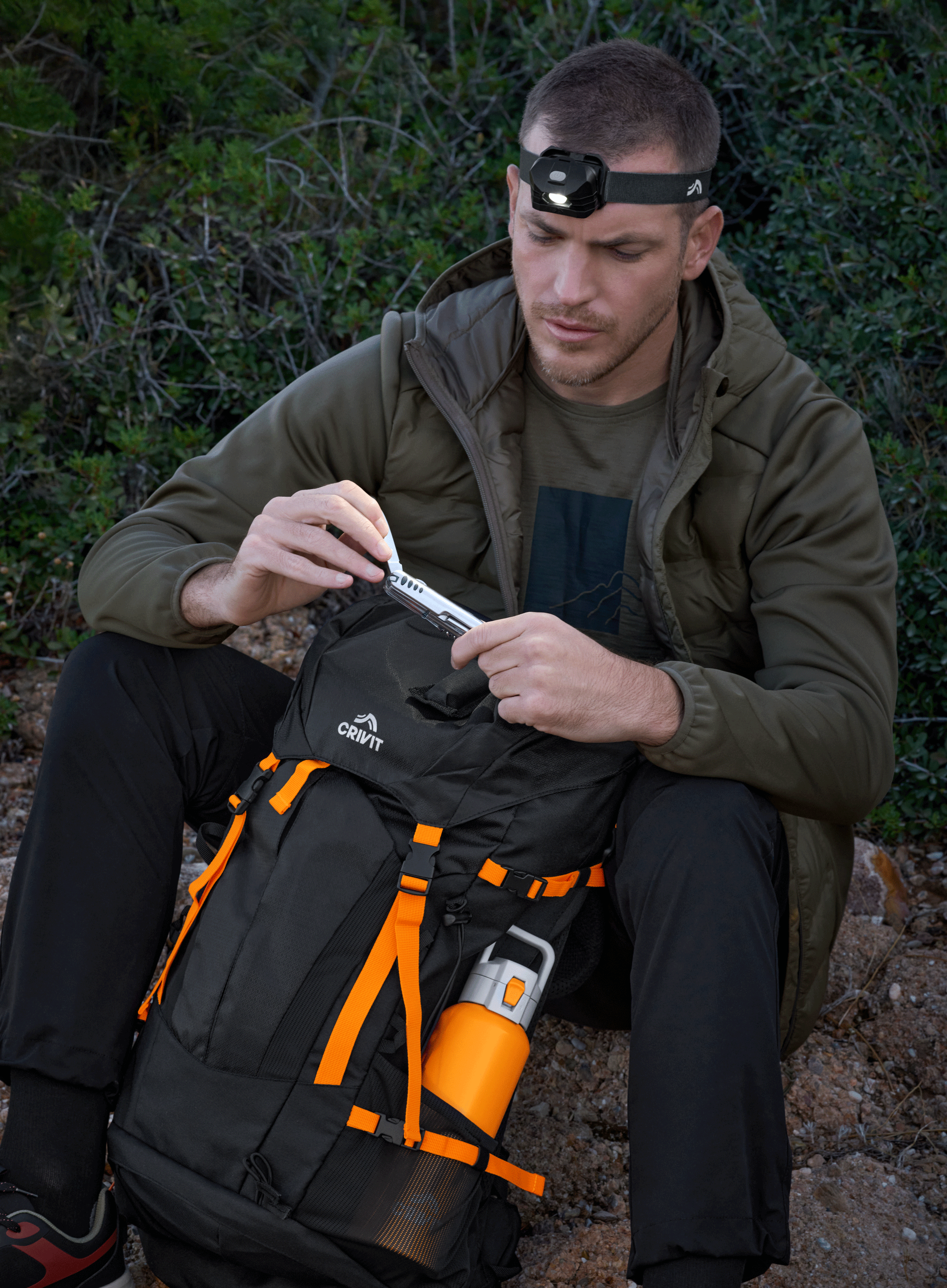 Homme avec une lampe frontale et un sac à dos de randonnée, tenant un couteau multifonction.