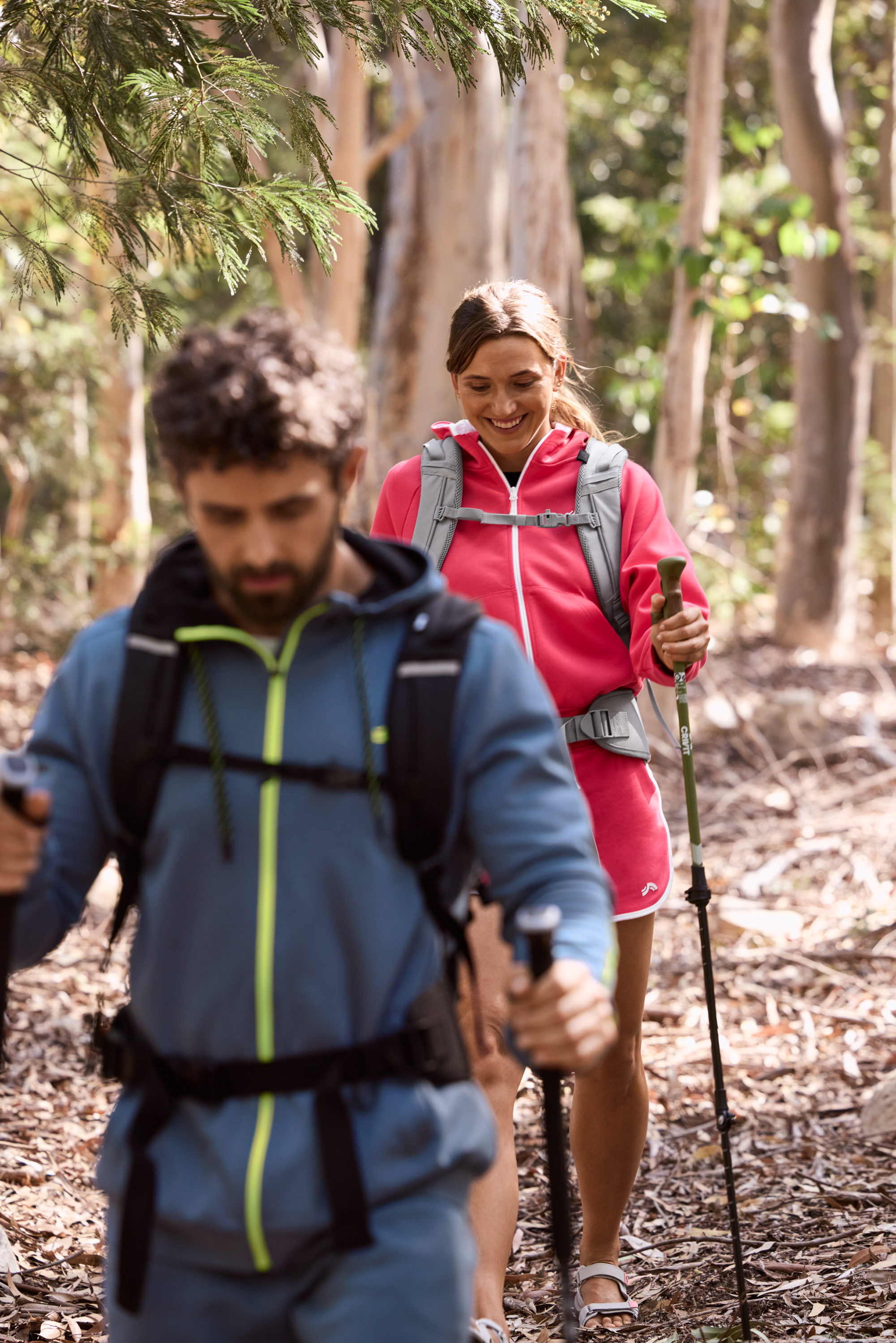 Deux randonneurs avec des bâtons de marche et des sacs à dos dans une forêt ensoleillée.