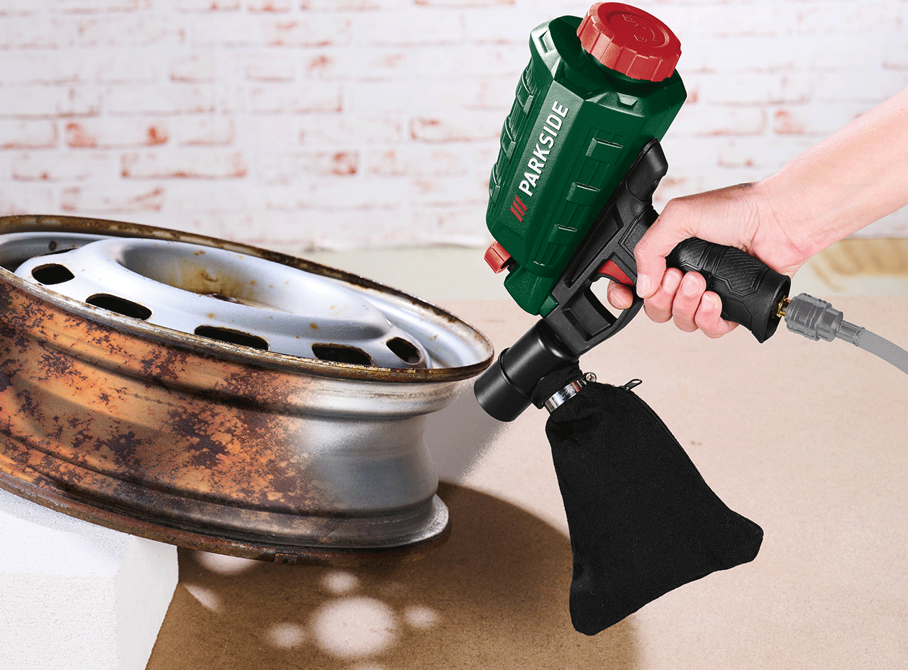 Pistolet de sablage manuel nettoyant une jante de voiture rouillée.