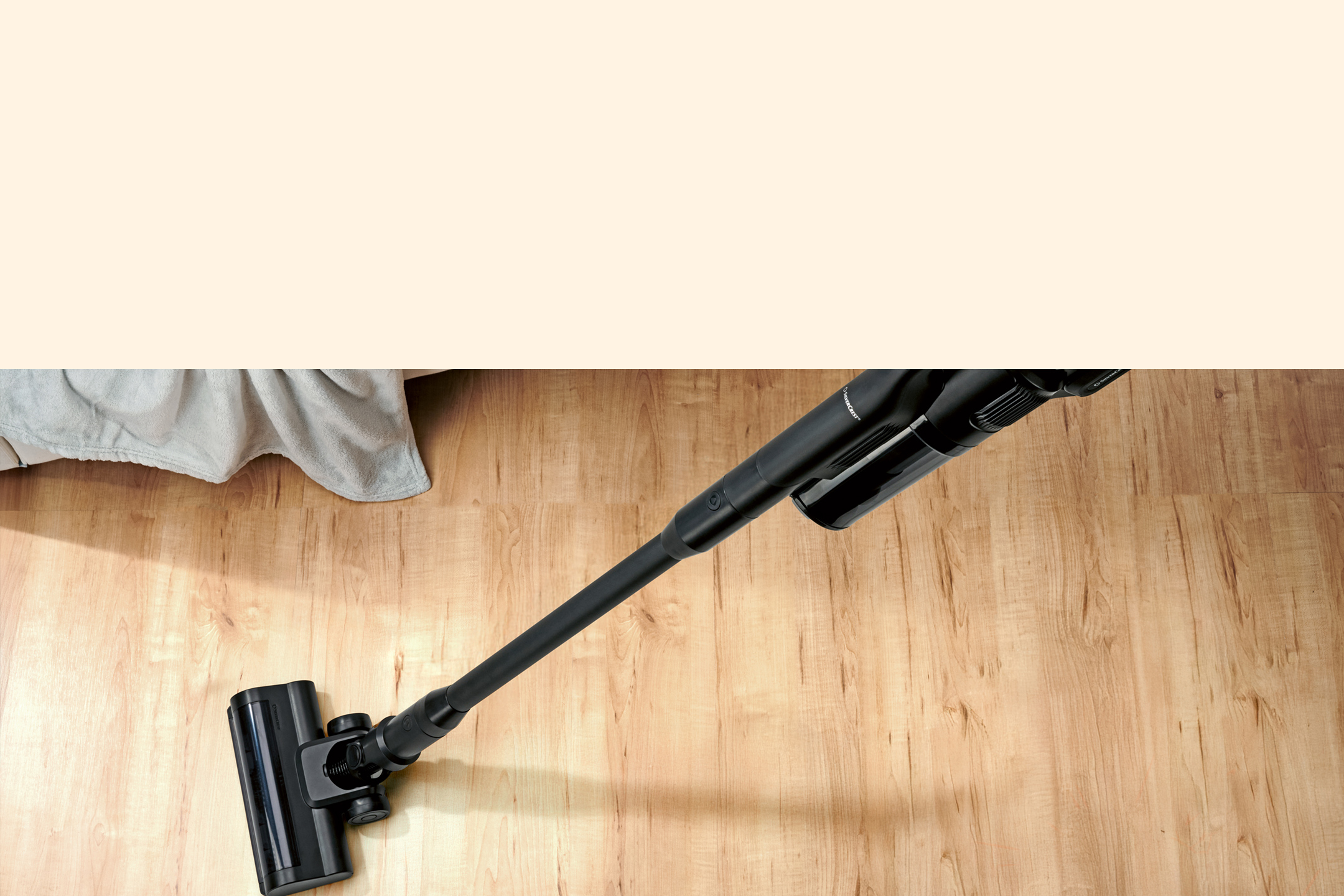 Aspirateur balai sans fil noir sur un sol en bois clair, près d'un canapé.