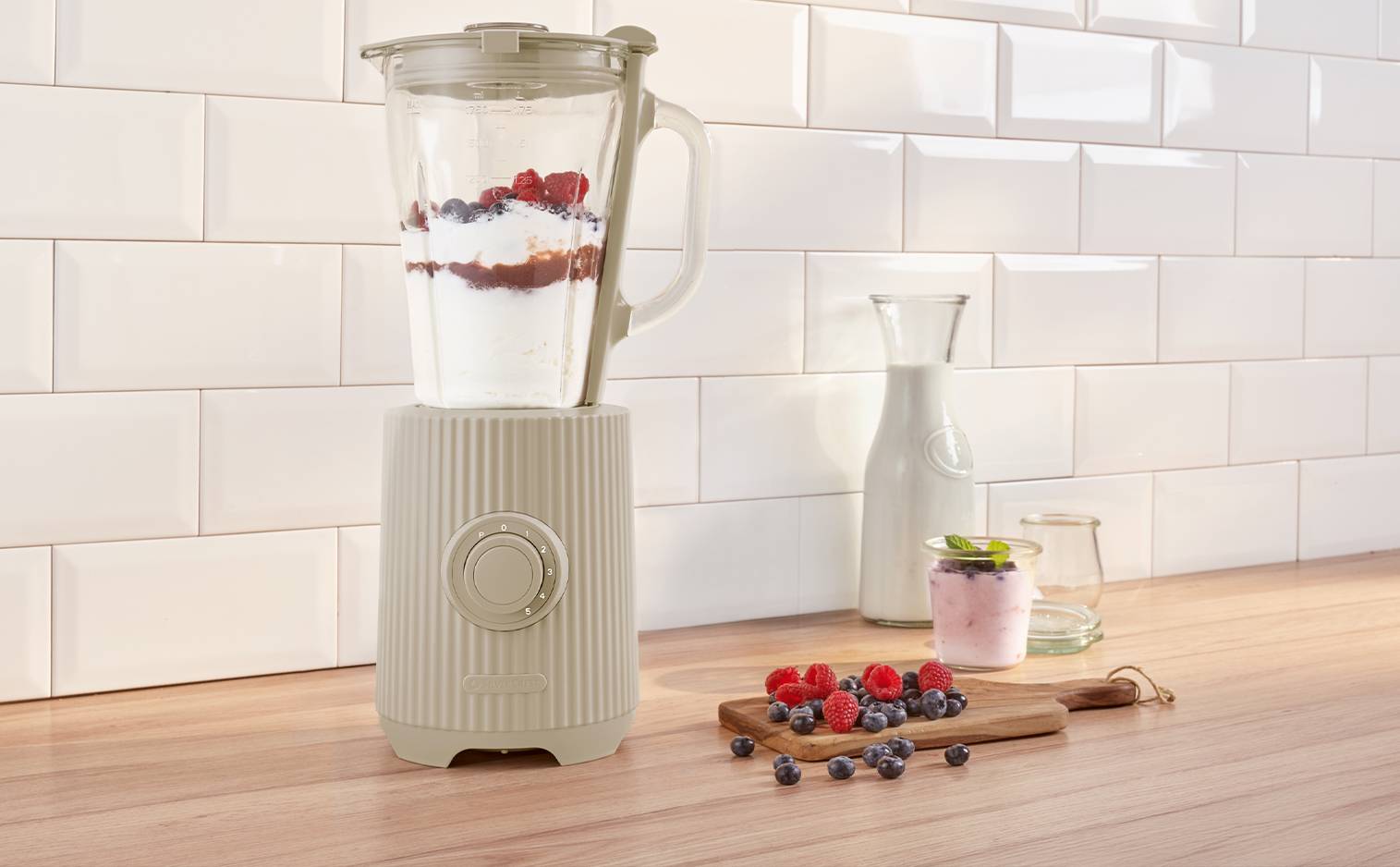 Mixeur de cuisine avec des fruits rouges et du yaourt sur un plan de travail en bois.