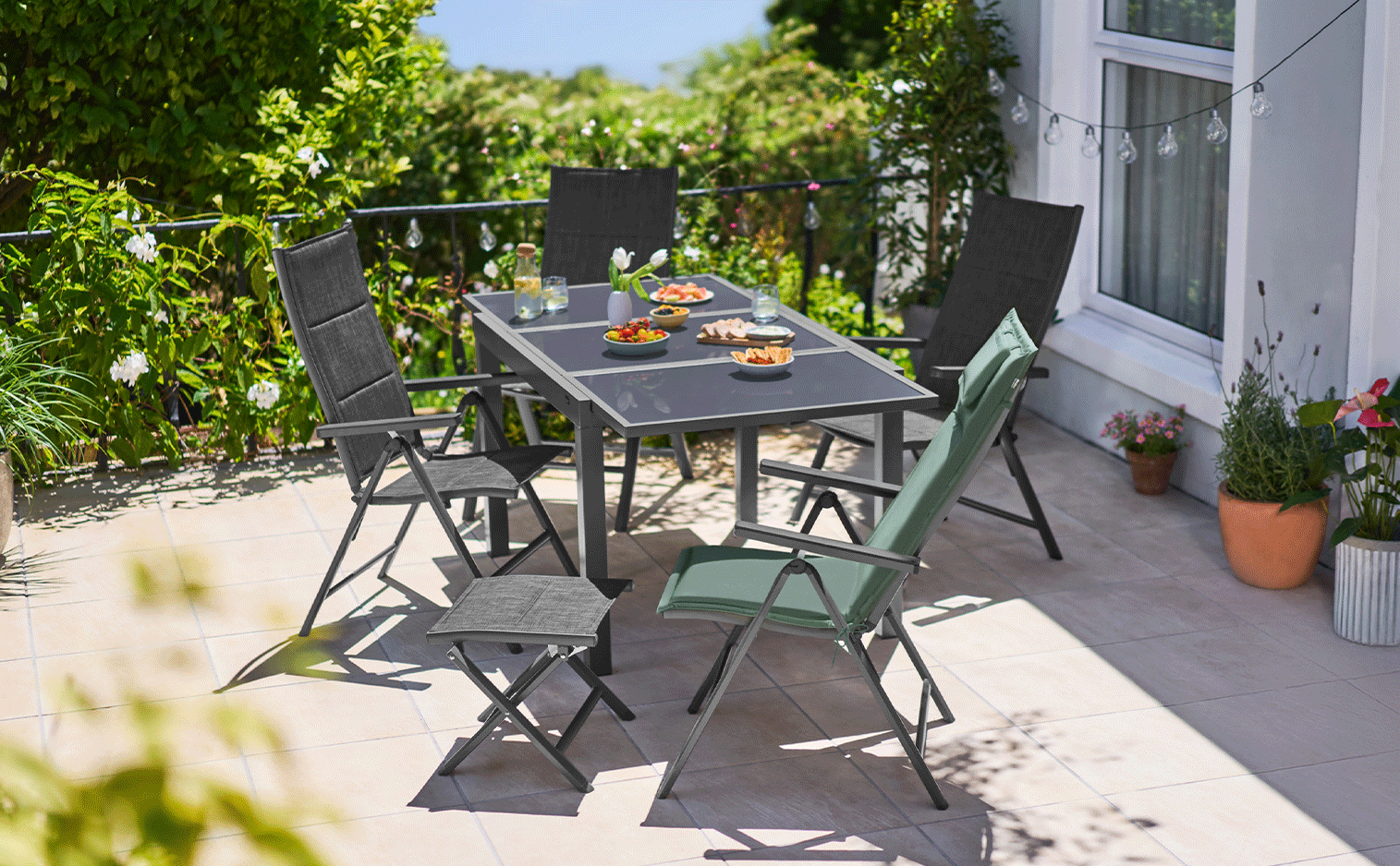 Ensemble de mobilier de jardin avec table et chaises, nourriture et boissons sur une terrasse ensoleillée.
