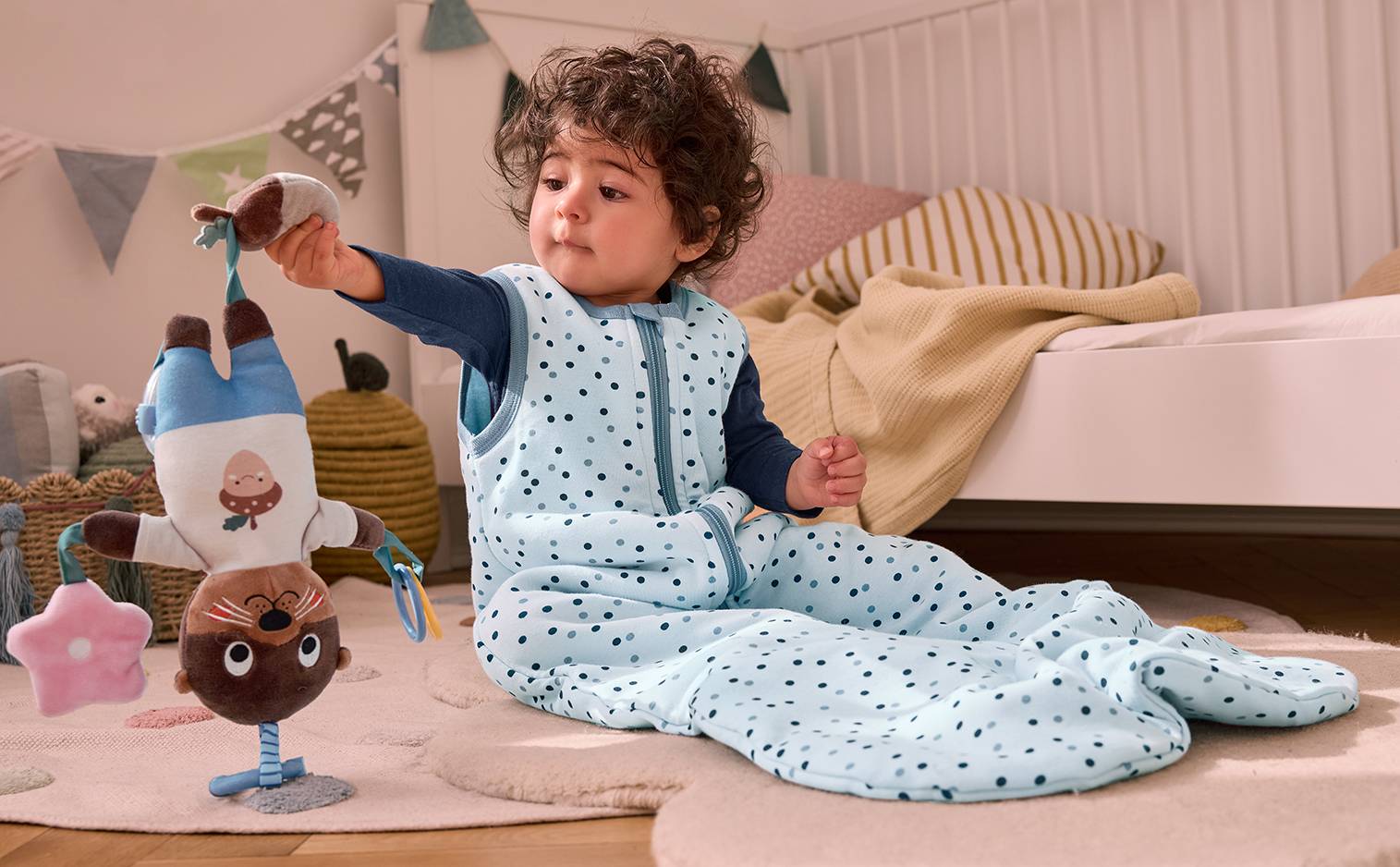 Bébé en gigoteuse à pois bleus jouant avec un hochet en forme d'écureuil.