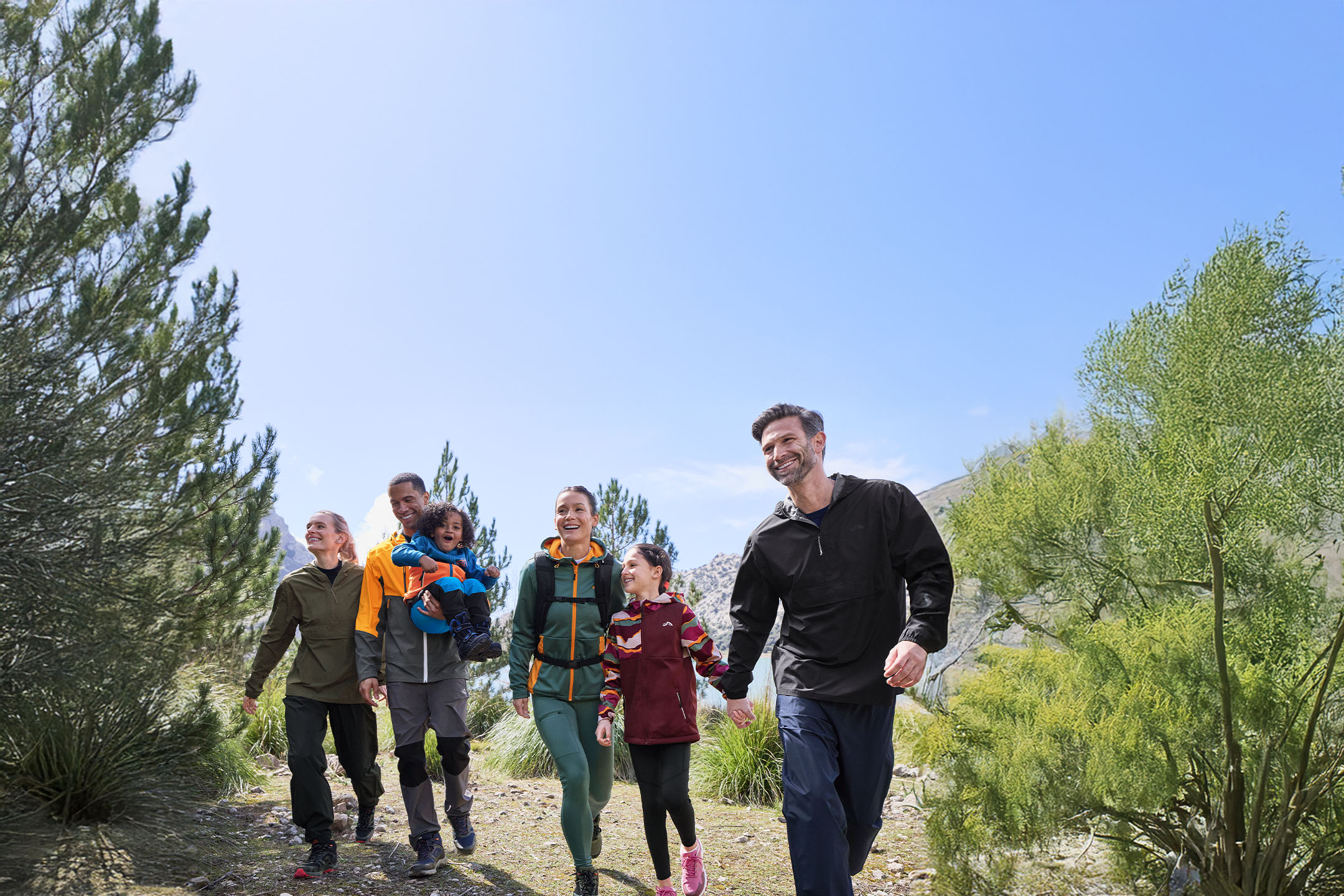Familles en tenue et chaussures de randonnée marchant sur un sentier forestier.