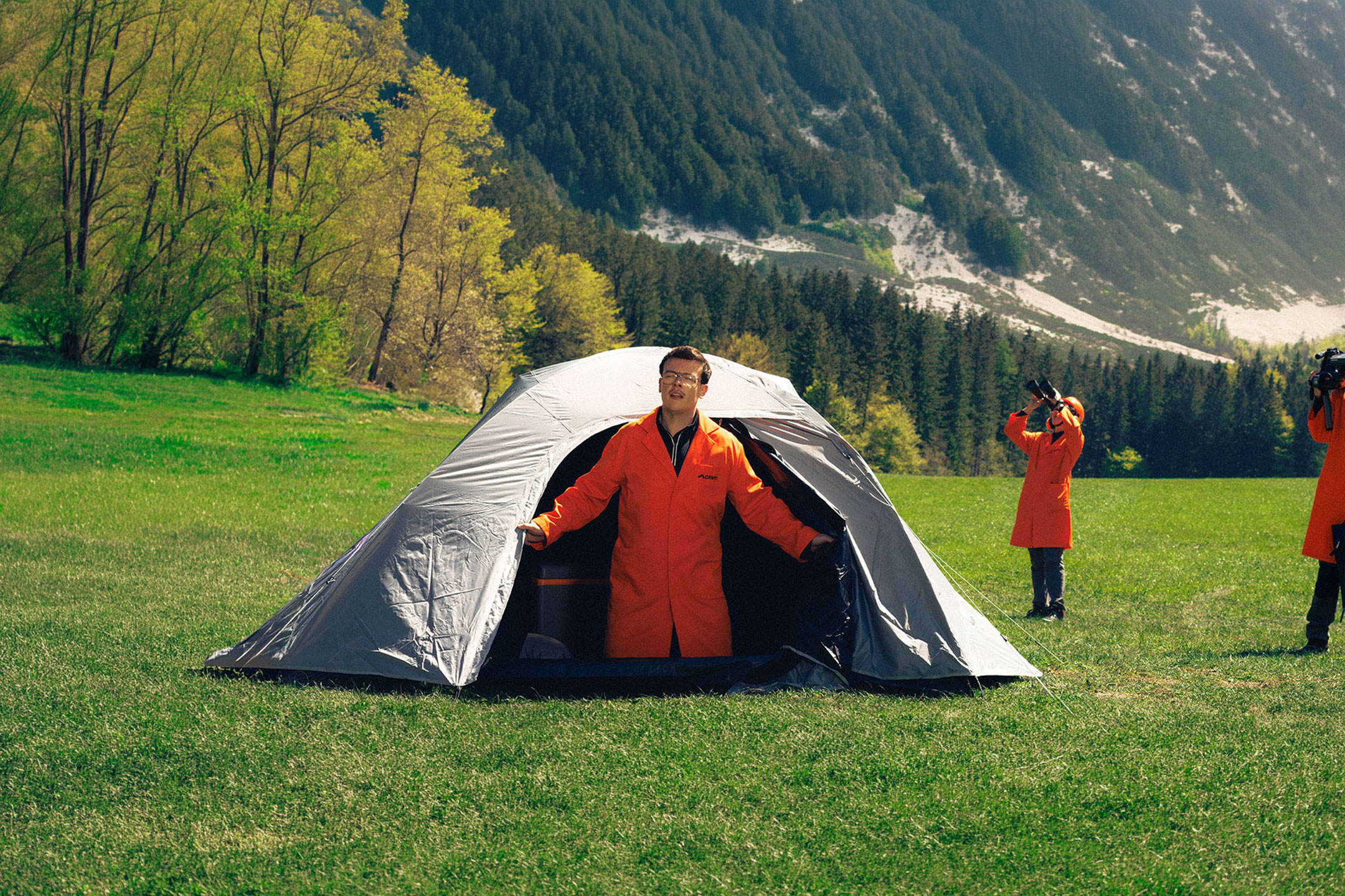 aiLabeling.aiLabelForImageAltText: Trois personnes en blouses oranges avec équipement de camping et d'observation dans une prairie.