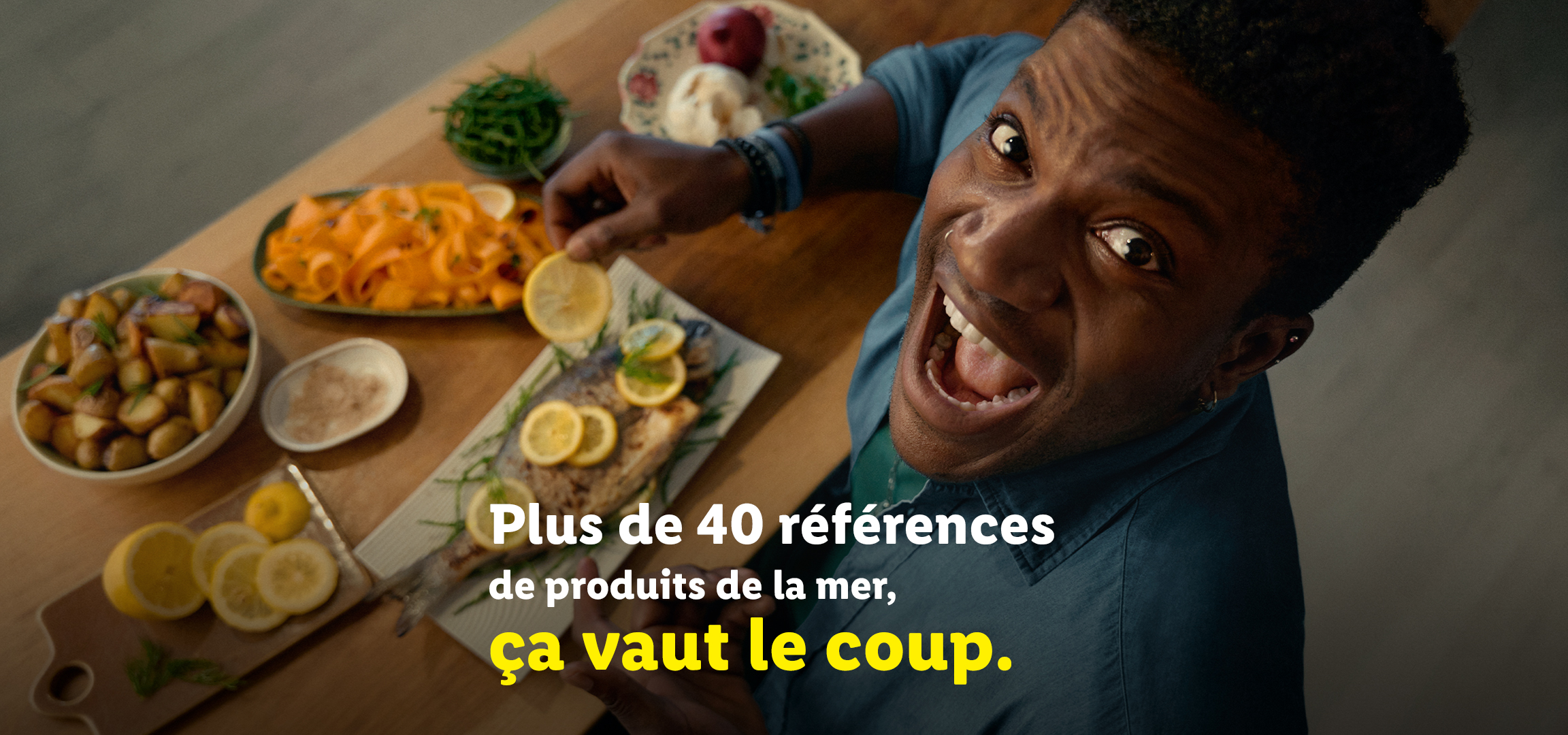 Un homme souriant avec des plats de fruits de mer et des pommes de terre, avec le texte 'Plus de 40 références de produits de la mer, ça vaut le coup.'