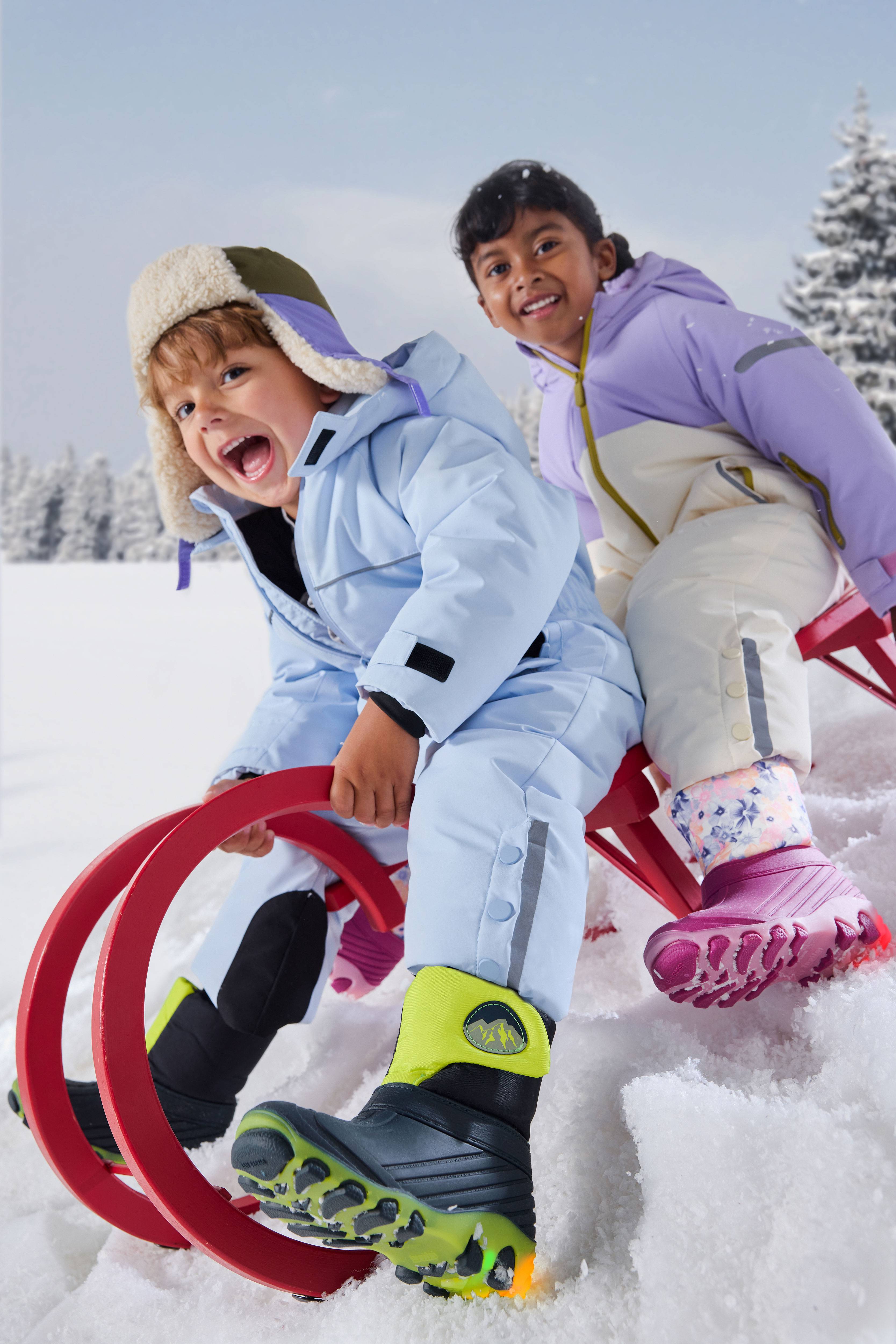Enfants joyeux en combinaison de neige et bottes d'hiver faisant de la luge.
