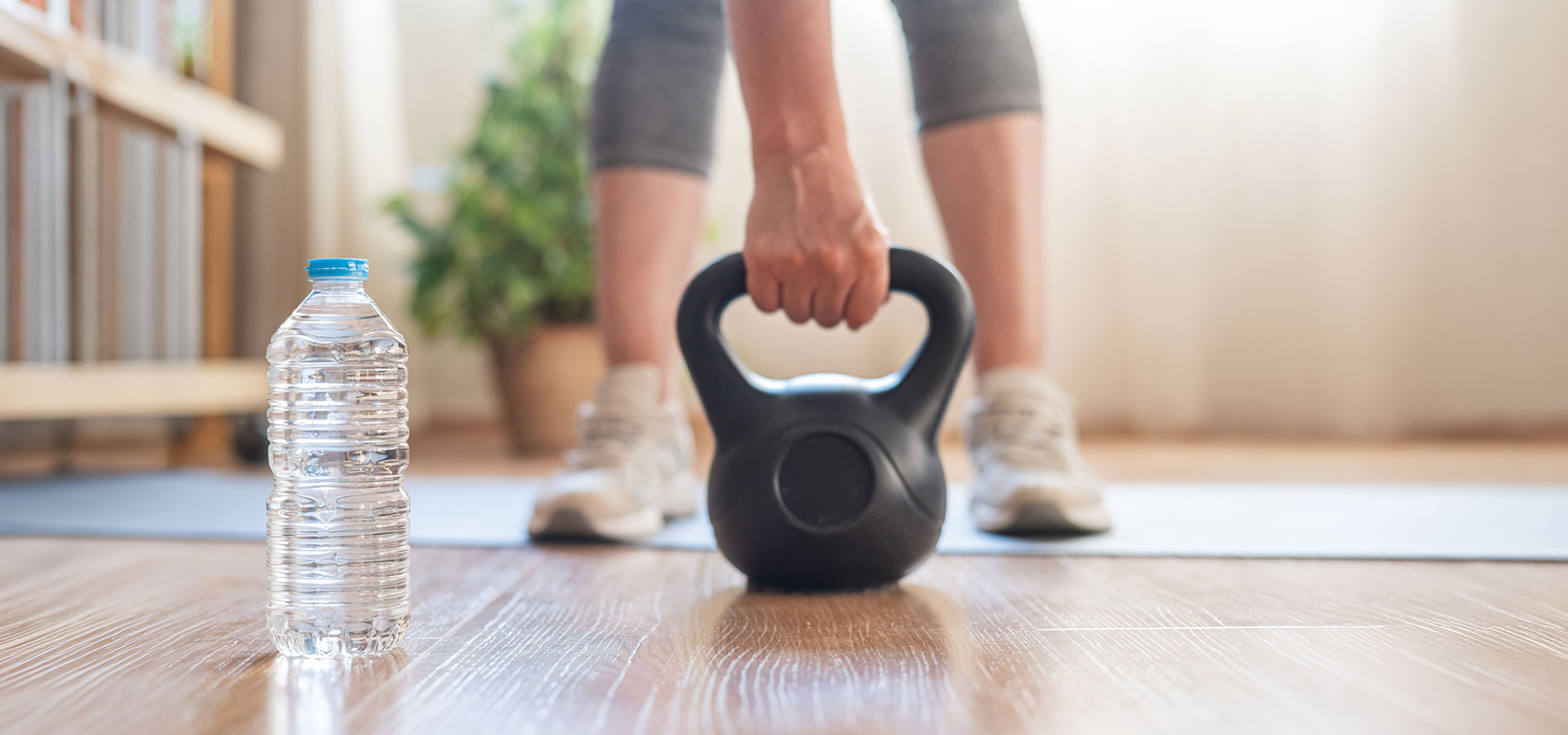 aiLabeling.aiLabelForImageAltText: Femme se prépare à s'entraîner avec un kettlebell et une bouteille d'eau sur un tapis de yoga.