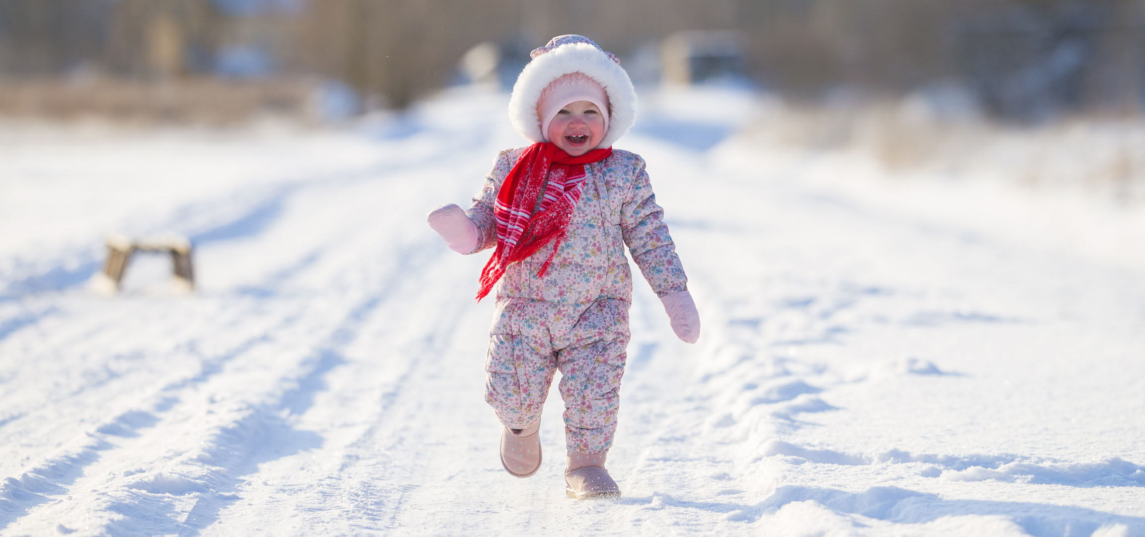 Petite fille joyeuse en combinaison d'hiver et écharpe courant sur un chemin enneigé.