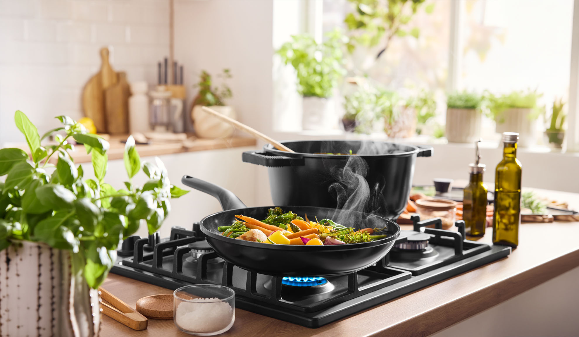 Légumes fumants cuisant dans une poêle et une casserole sur une plaque de cuisson à gaz dans une cuisine lumineuse.