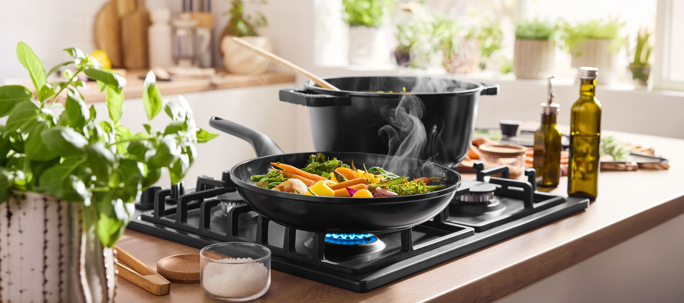 Cuisson de légumes dans une poêle sur une plaque de cuisson à gaz, avec une casserole et de l'huile d'olive à proximité.