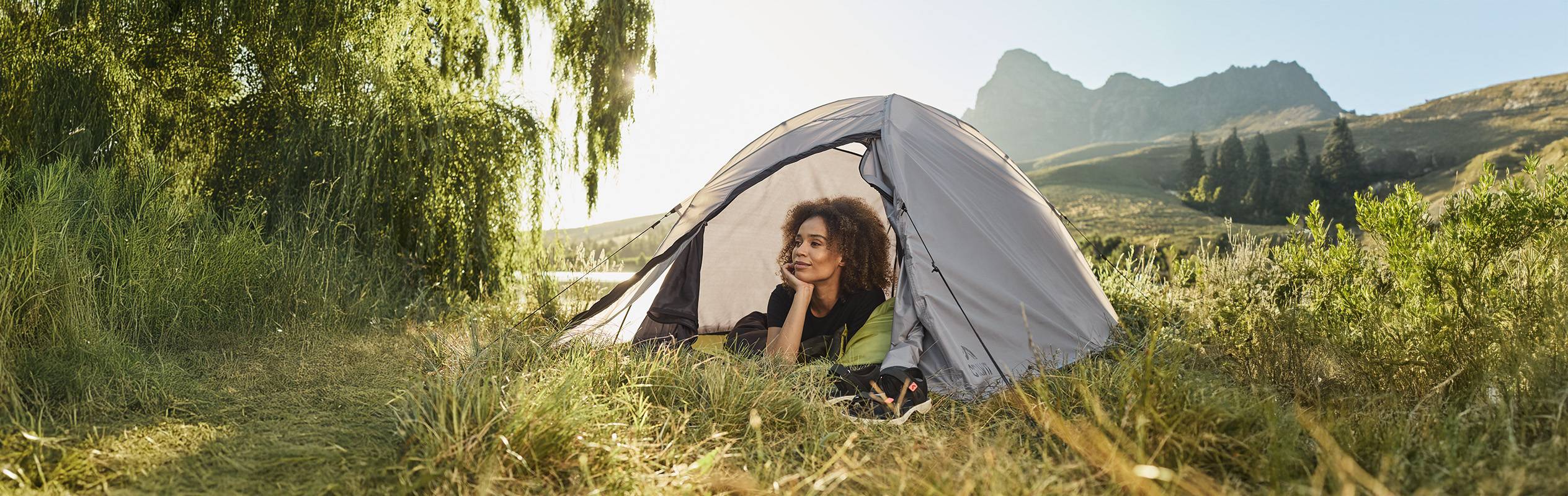 Une femme se repose dans une tente de camping au milieu d'un paysage montagneux.