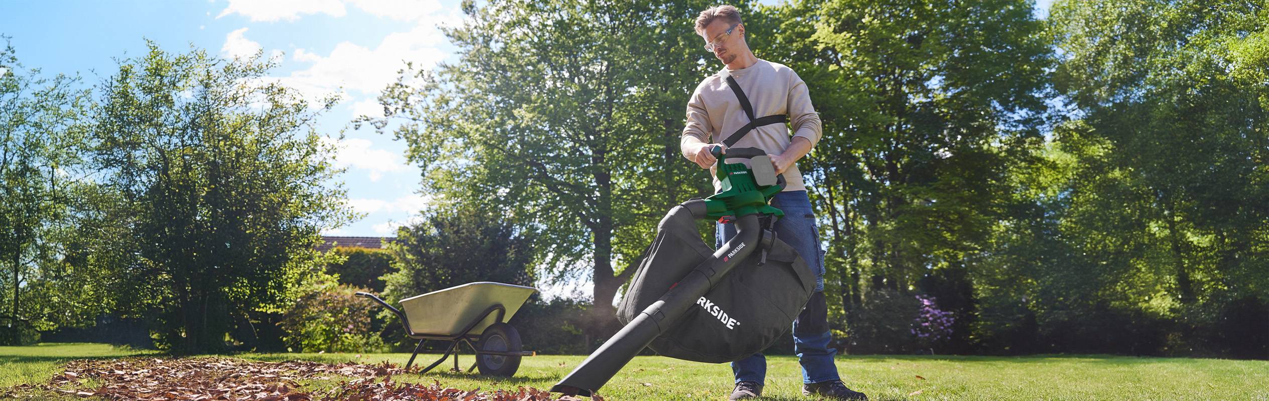 Un homme utilise un souffleur de feuilles Parkside pour nettoyer les feuilles mortes dans un jardin.