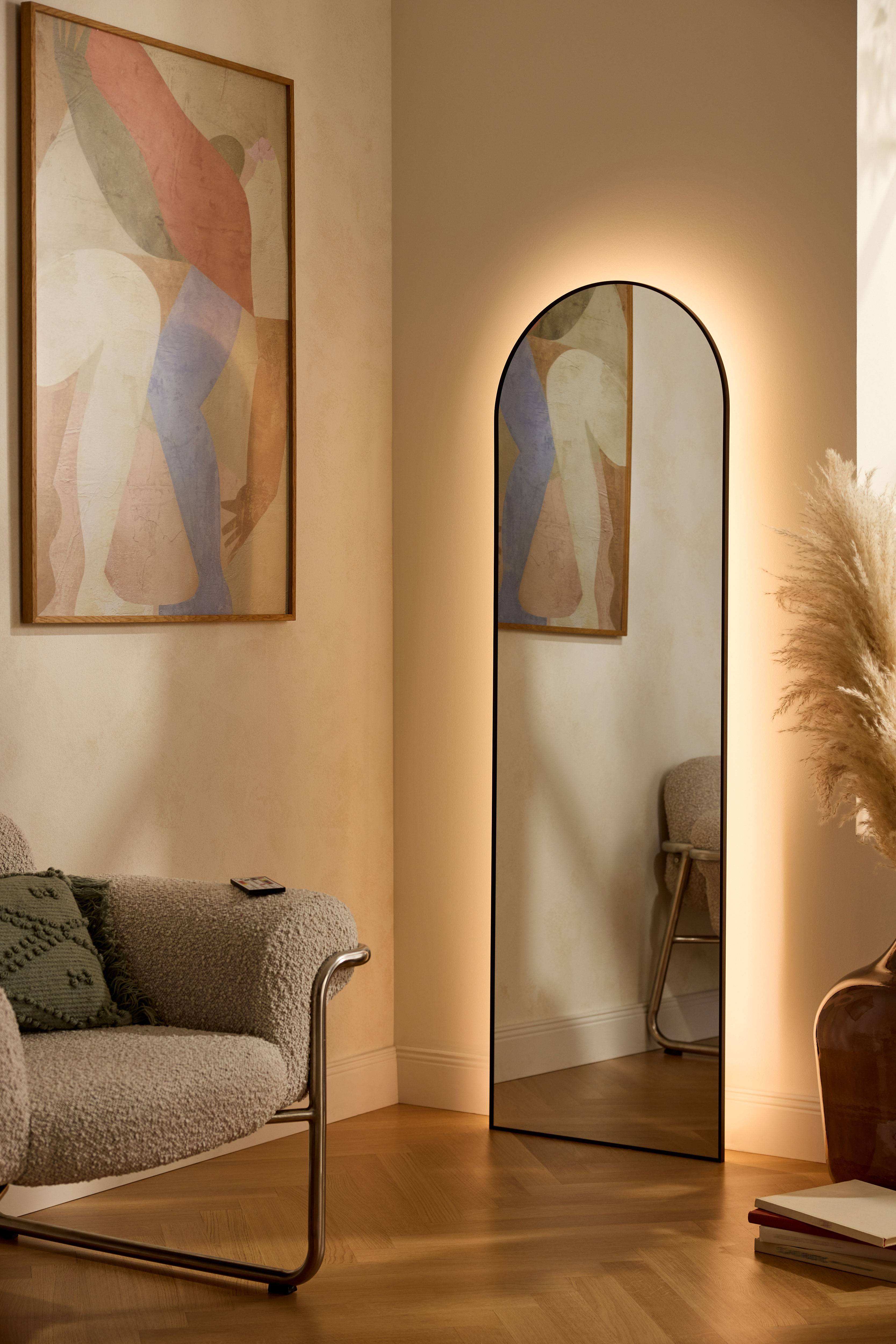 Miroir éclairé et tableau abstrait dans un salon moderne avec fauteuil et herbe de la pampa.