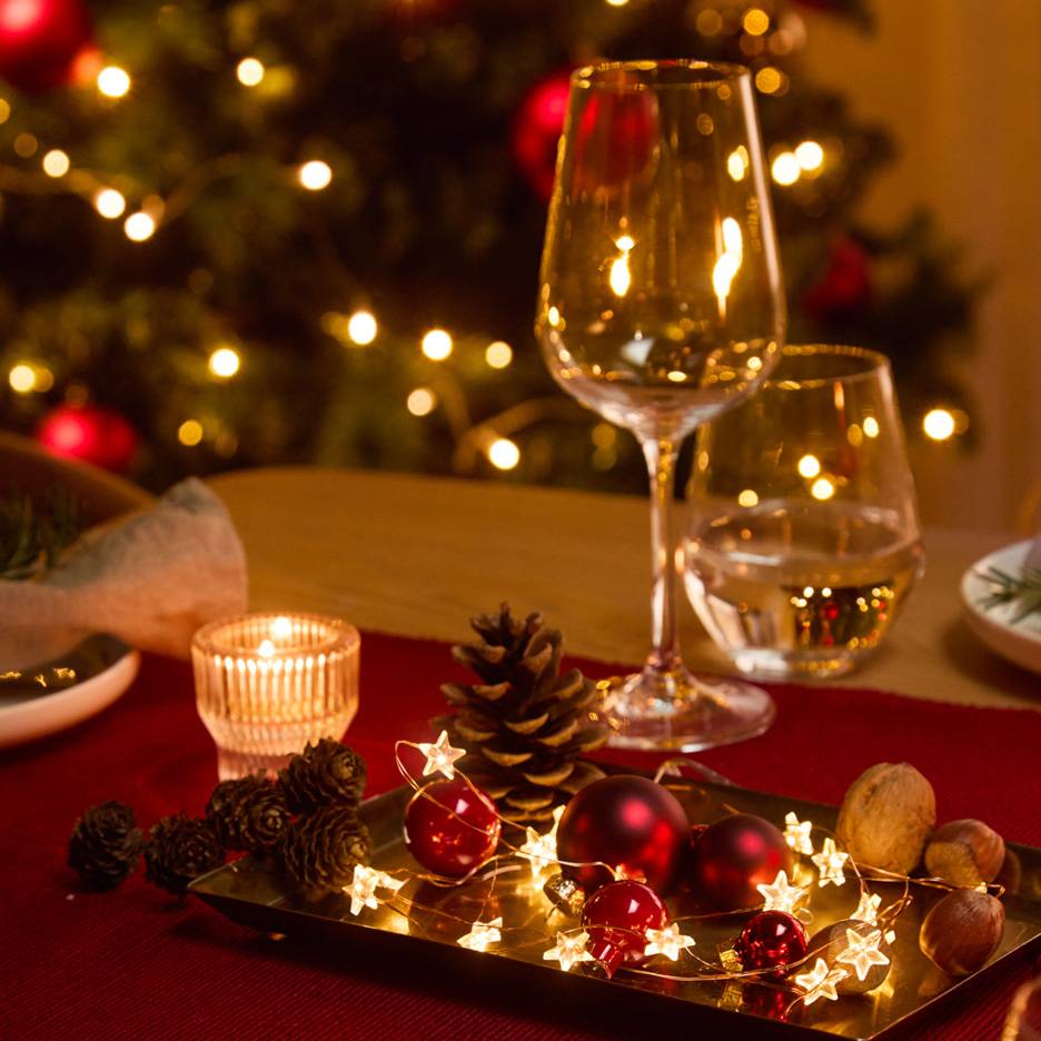 Décoration de table de Noël avec verres, bougie et guirlande lumineuse.