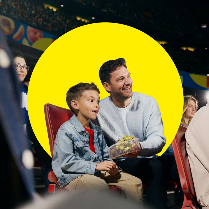 Père et fils savourent des fruits dans un contenant lors d'un événement sportif.
