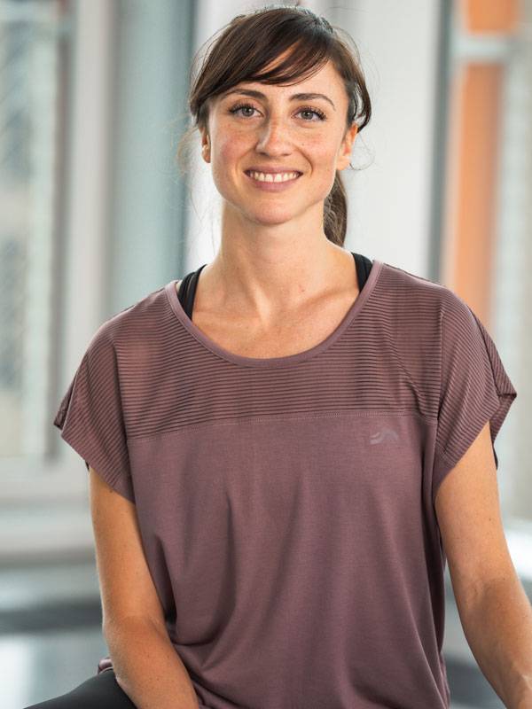 Femme souriante portant un haut de sport violet à manches courtes.