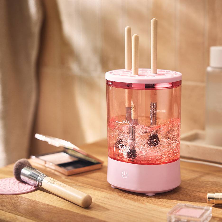 Nettoyeur de pinceaux de maquillage rose avec pinceaux dans l'eau pétillante.