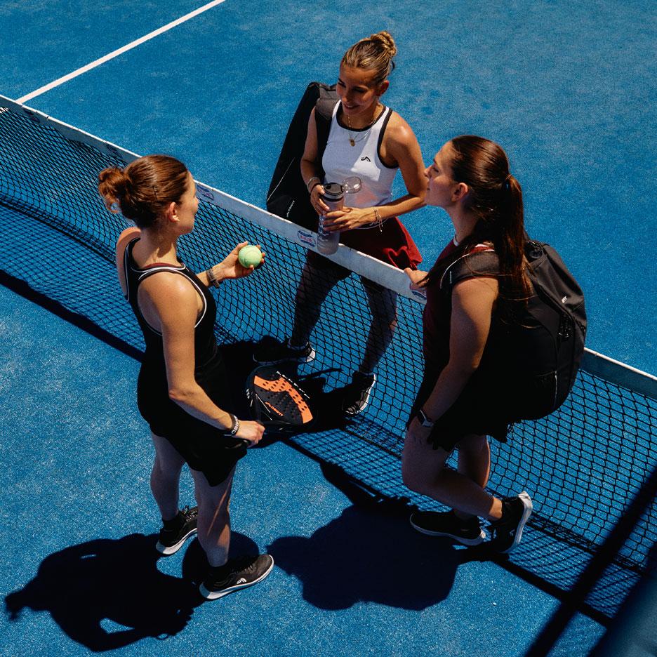 Agostina Bigotti et deux autres joueuses en tenue de sport CRIVIT se tiennent ensemble près du filet de padel sur un court bleu après le match.