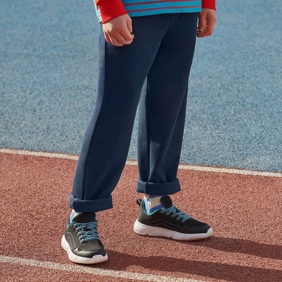 Pantalon de survêtement bleu marine et baskets noires à lacets bleus sur une piste de course.