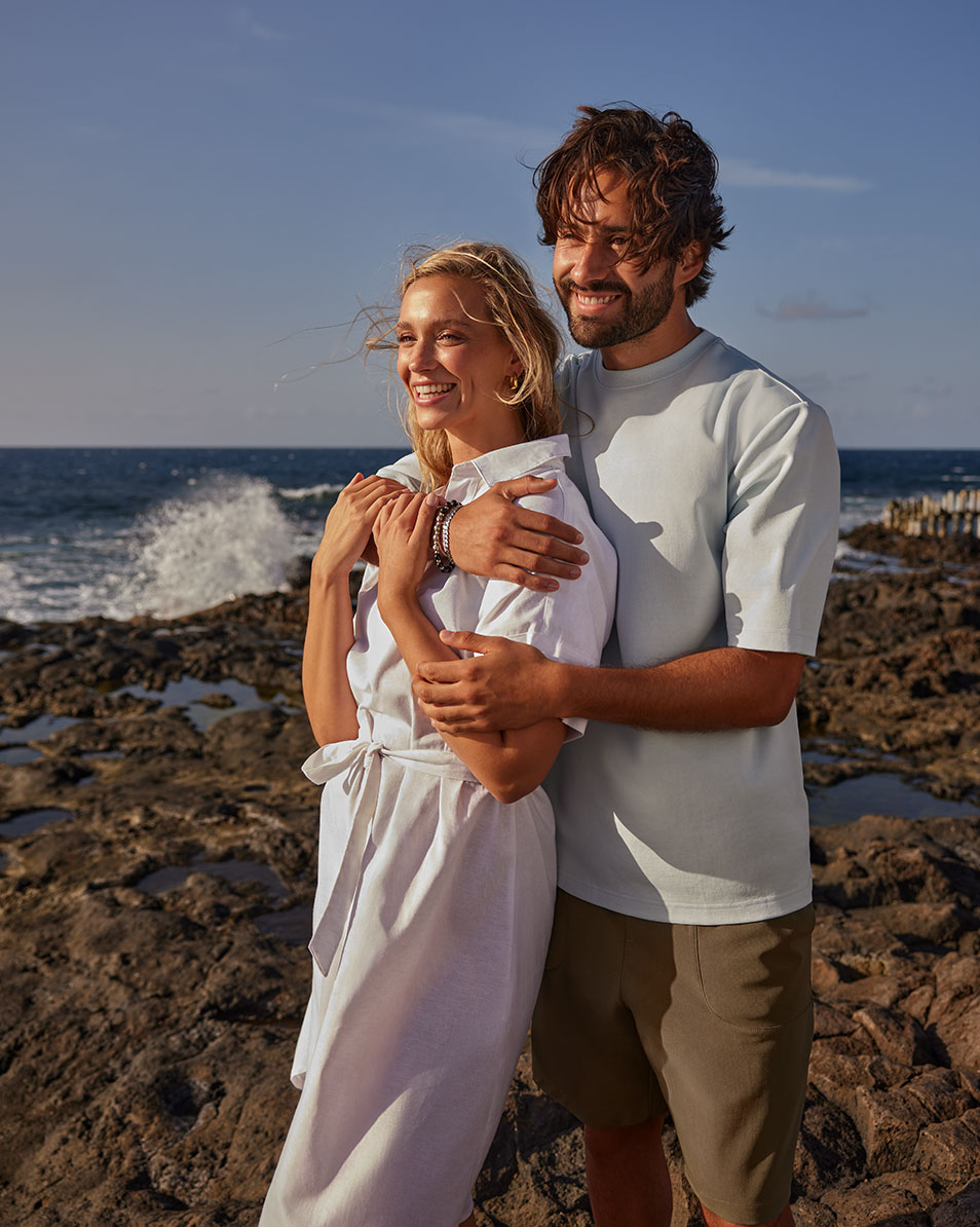 Couple sur la plage, femme en robe blanche, homme en T-shirt bleu clair et short.