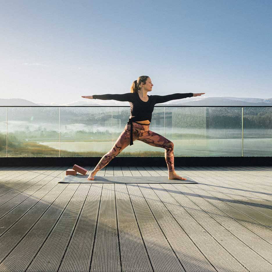 Femme en legging et haut de sport faisant du yoga sur une terrasse avec vue.