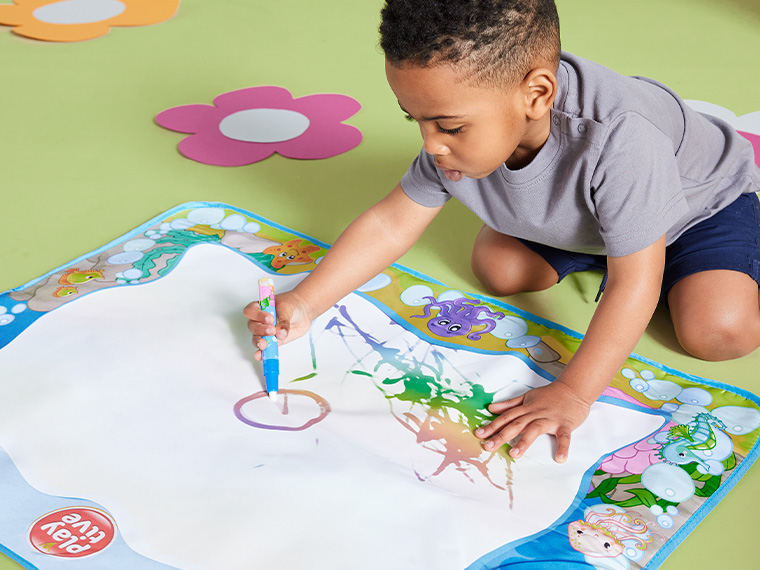 Un jeune garçon utilise un tapis à dessin Play-Doh aquatique pour créer des œuvres d'art colorées.