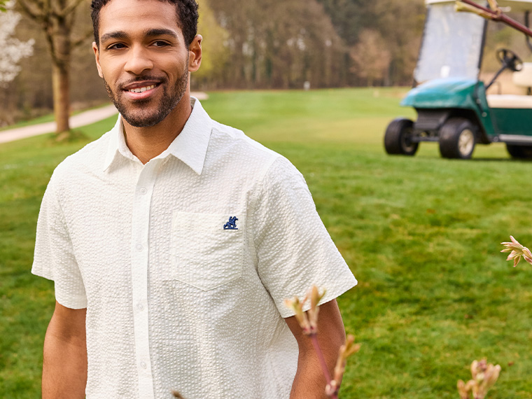 Un homme souriant porte une chemise blanche à motif texturé de la marque Southern Tide sur un terrain de golf.