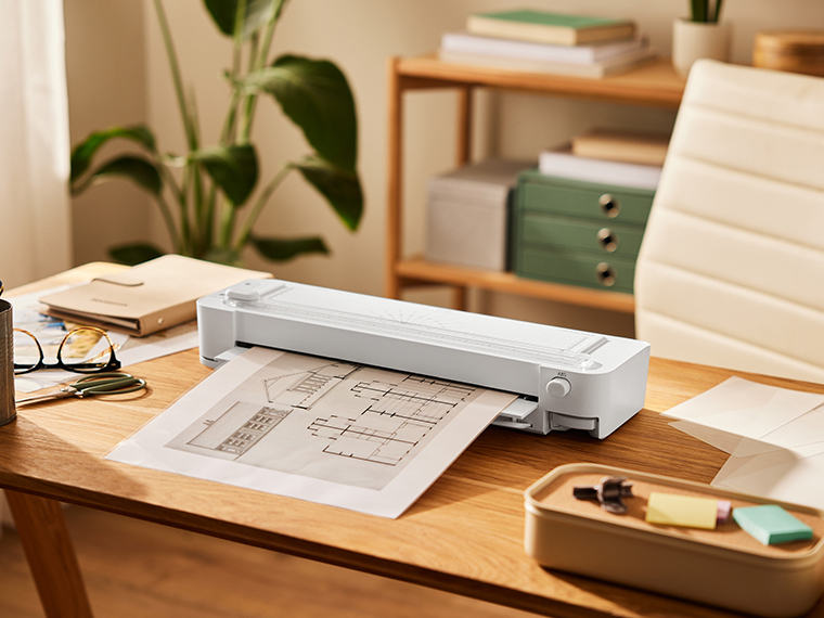 Une découpeuse de papier compacte et blanche est posée sur un bureau en bois, prête à l'emploi.